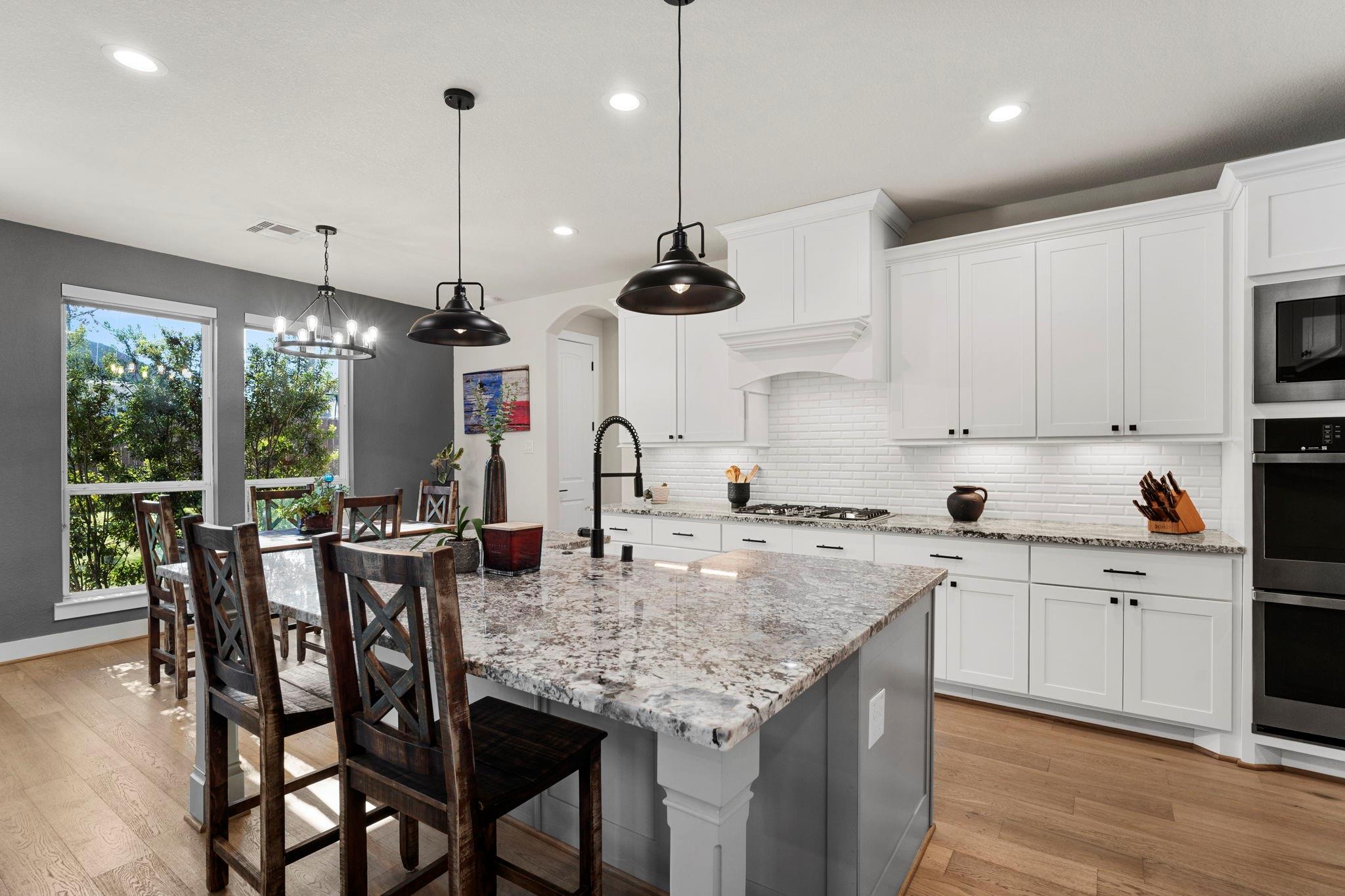 Bright kitchen with white cabinets, a large granite island, and dark wood bar stools by tall windows.