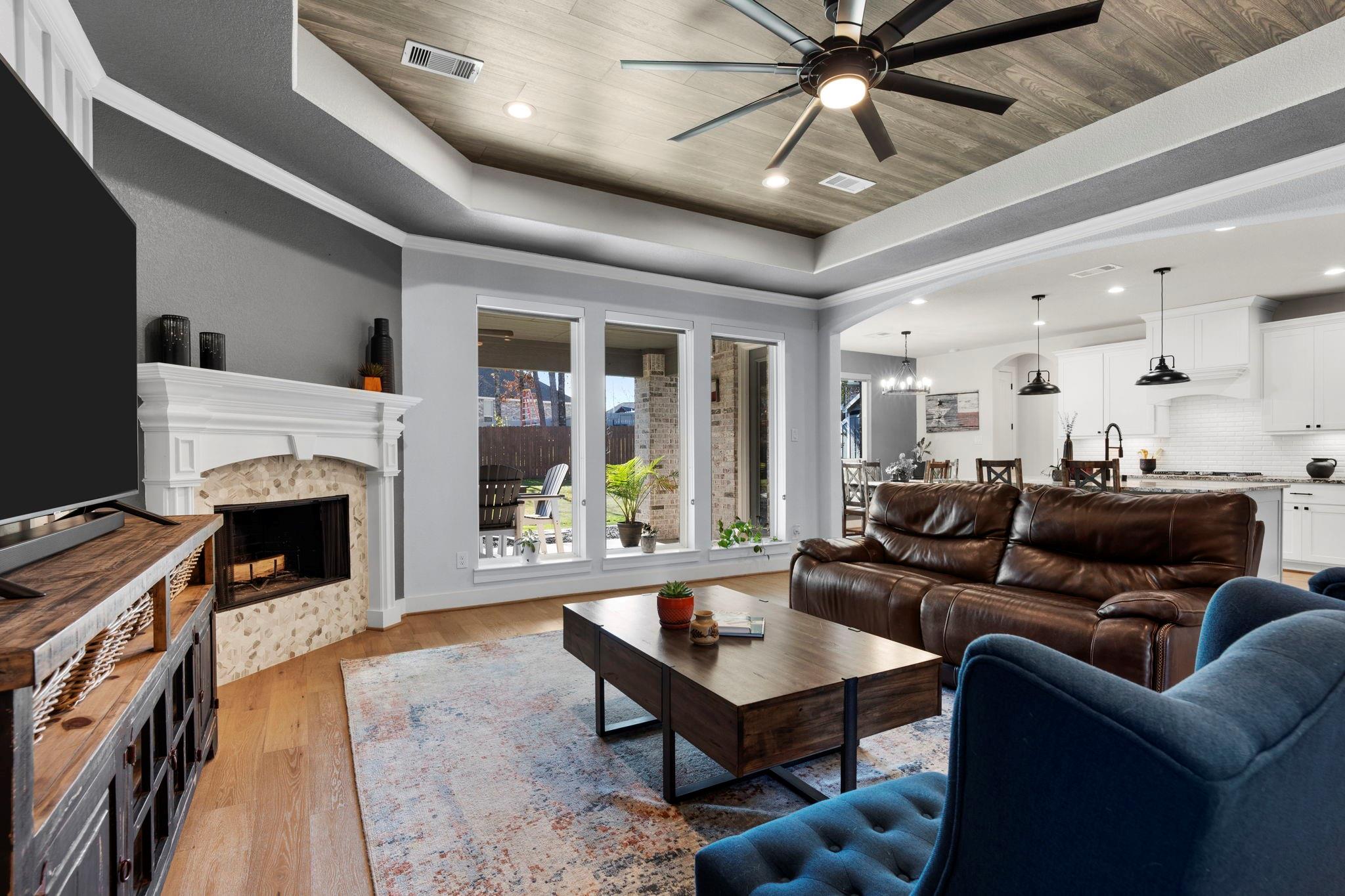 Living room with a stone fireplace, wood-inset tray ceiling, and open view into the white kitchen.