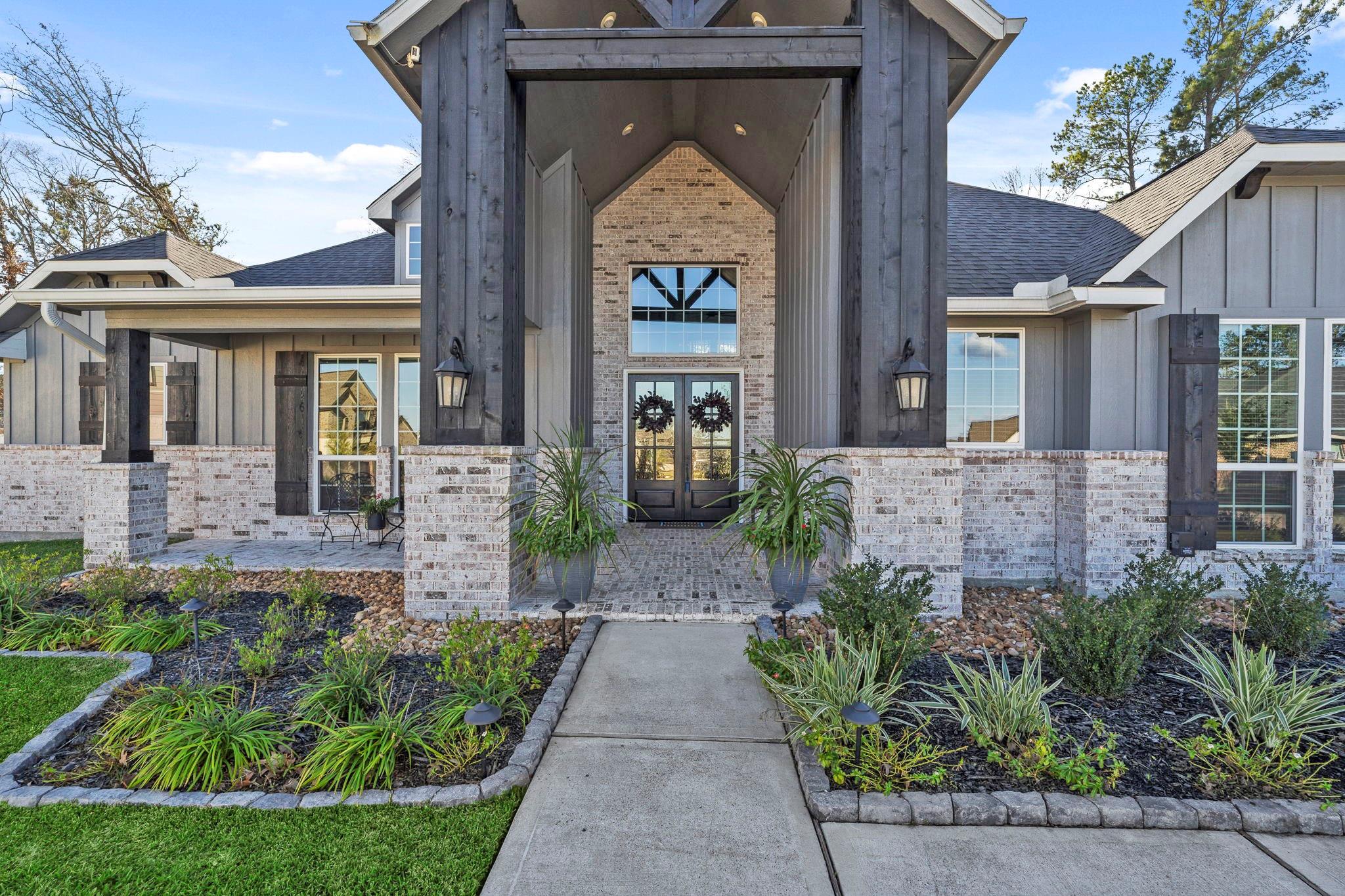 Gray-and-brick home with a tall covered entry, glass double doors, and landscaped front garden.
