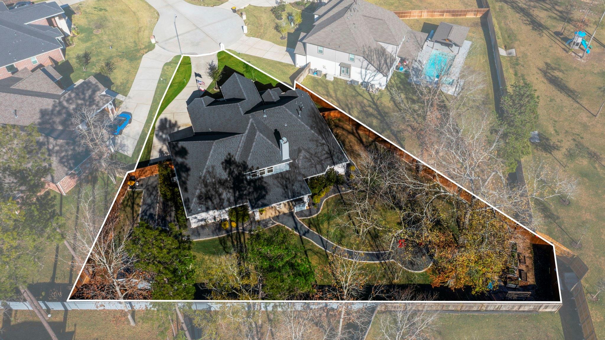 Aerial view of a large dark-roofed home and landscaped lot outlined against neighboring properties.