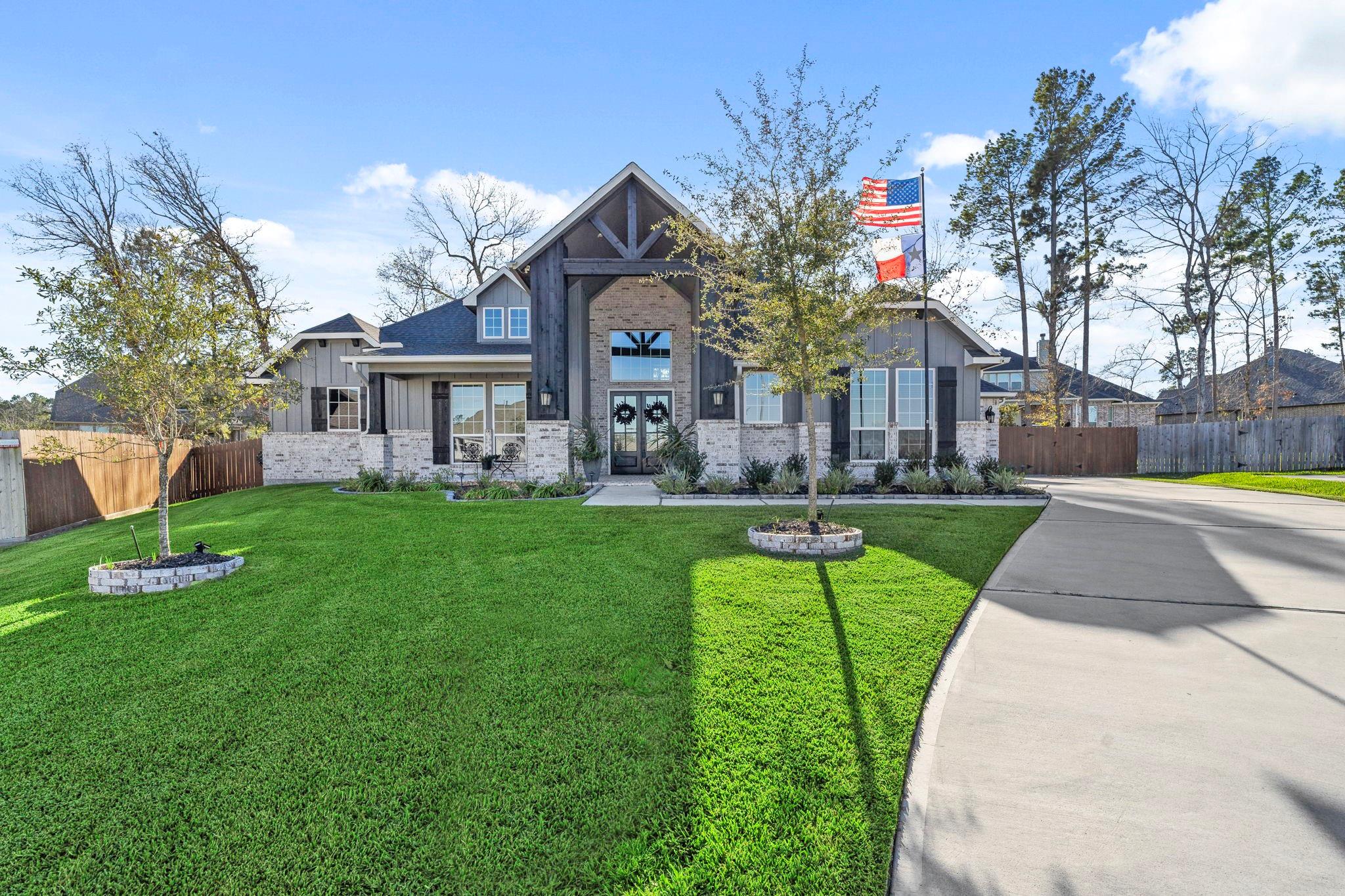 Gray-and-brick home with a timber-trimmed gable, broad lawn, curved driveway, and flags.