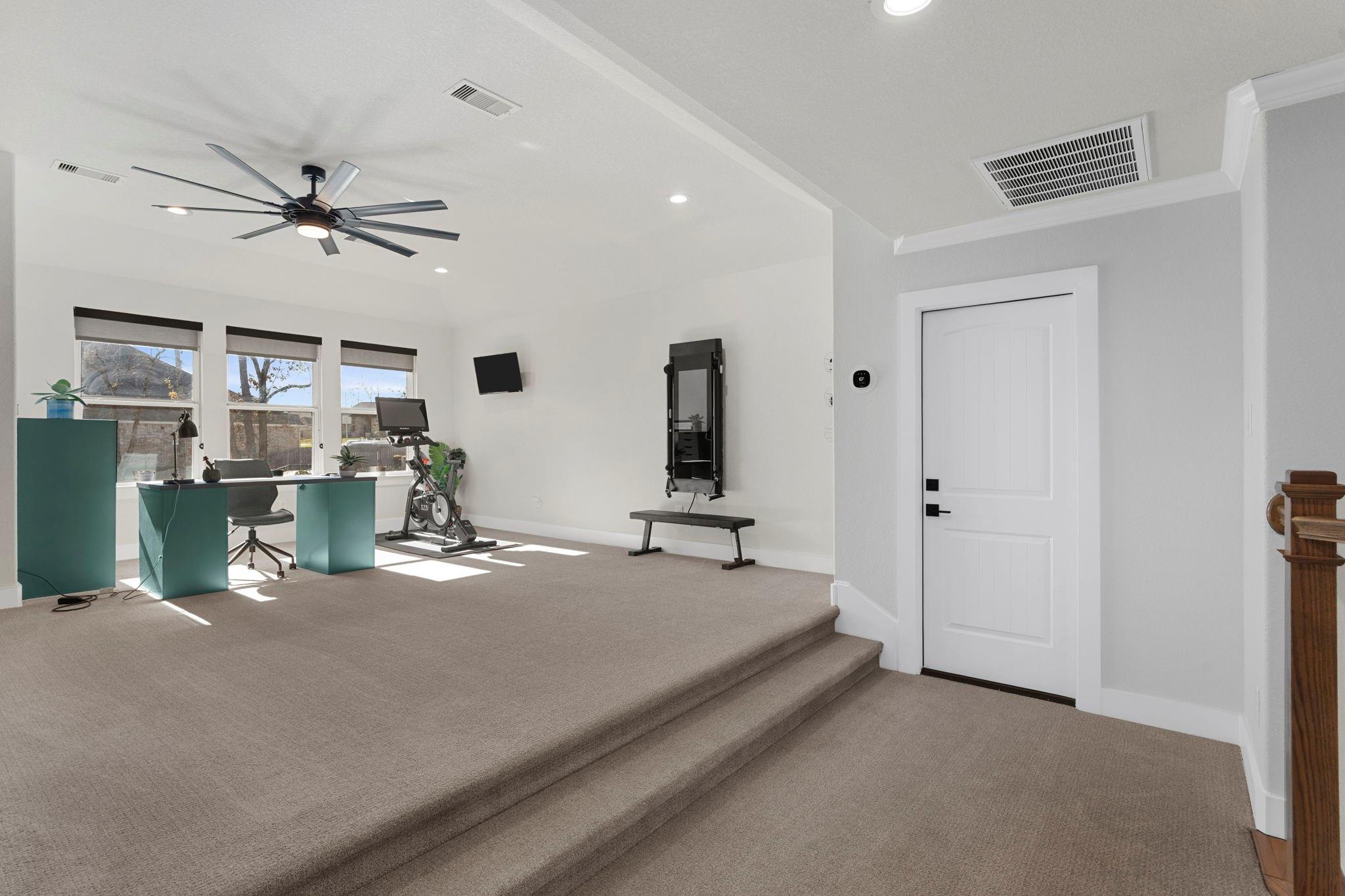 Home gym with an exercise bike, workout bench, and desk on a raised carpeted platform.