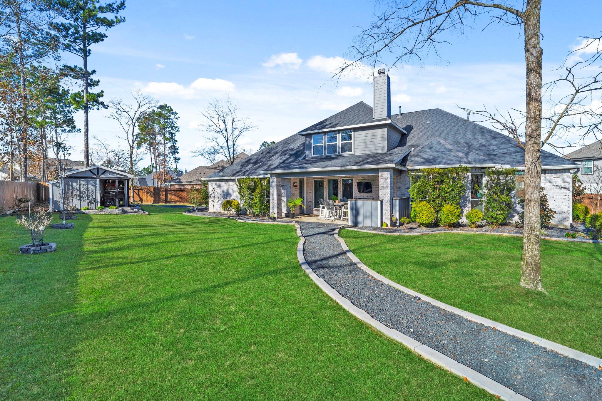 Two-story brick home with a covered patio, curved gravel path, and broad green backyard.