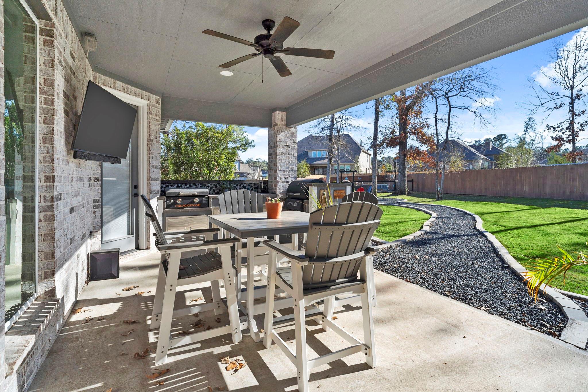Covered patio with dining furniture, a Blackstone grill, and a curved gravel path beside the lawn.