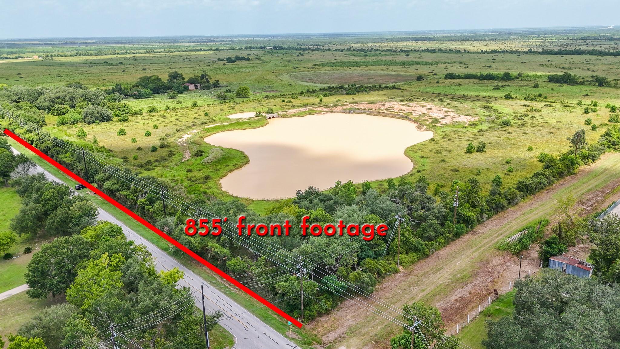 Aerial view of rural land with a large pond and road frontage marked by a red line.