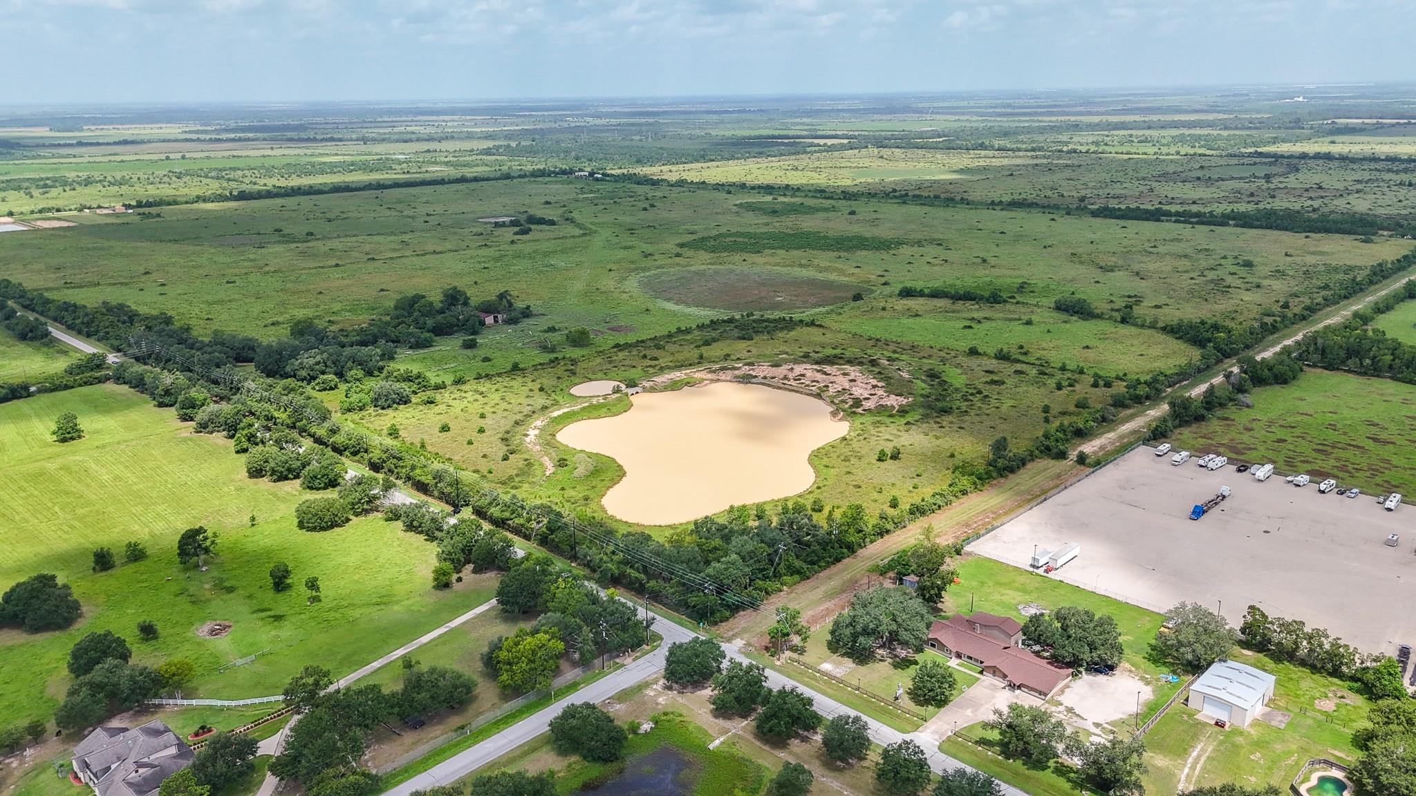 Aerial view of open land with a large pond, fields, and scattered homes.