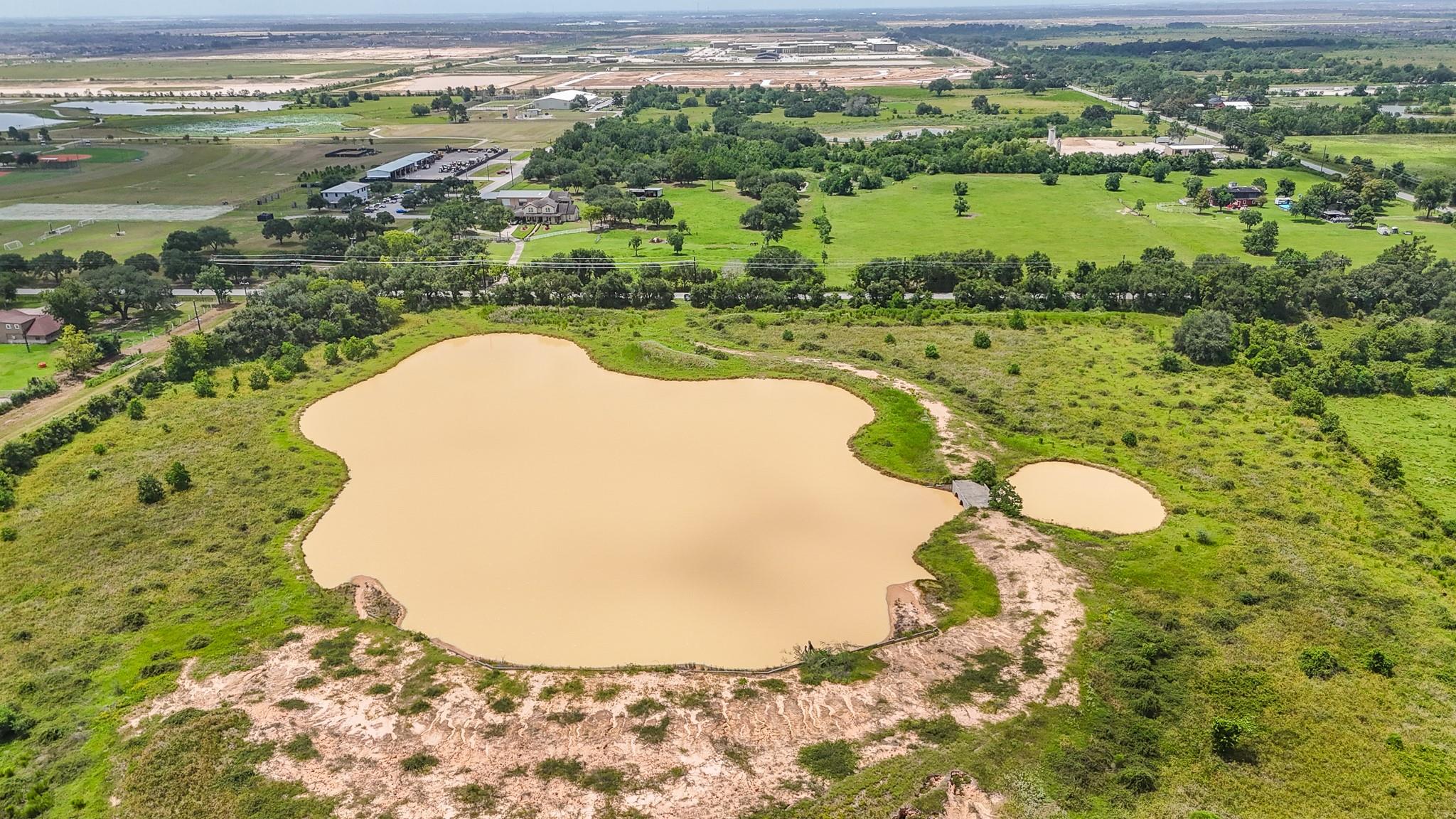 Aerial view of green acreage with two muddy ponds and scattered trees.