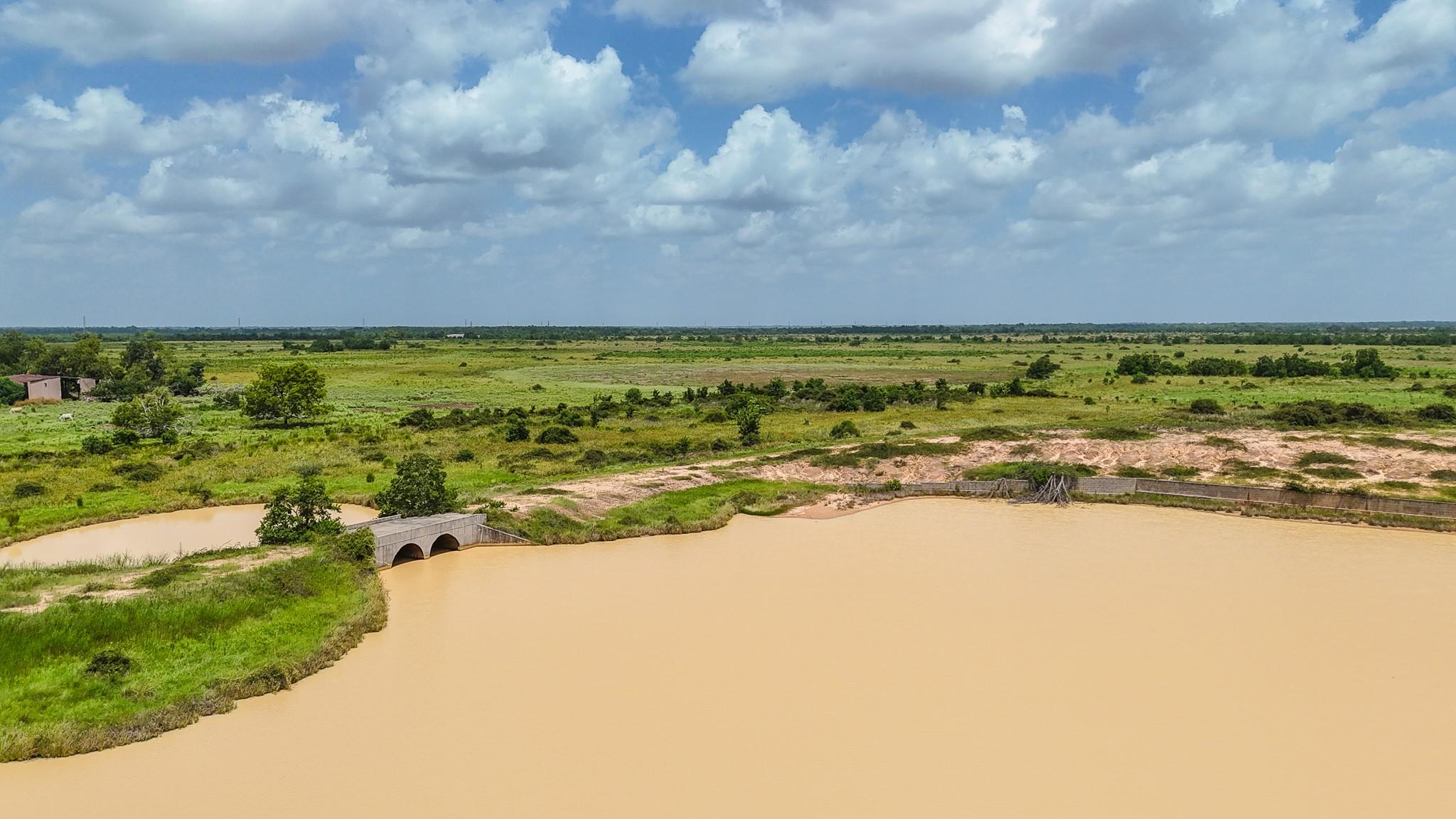 Open acreage and a large pond, with a small concrete bridge and distant tree line.