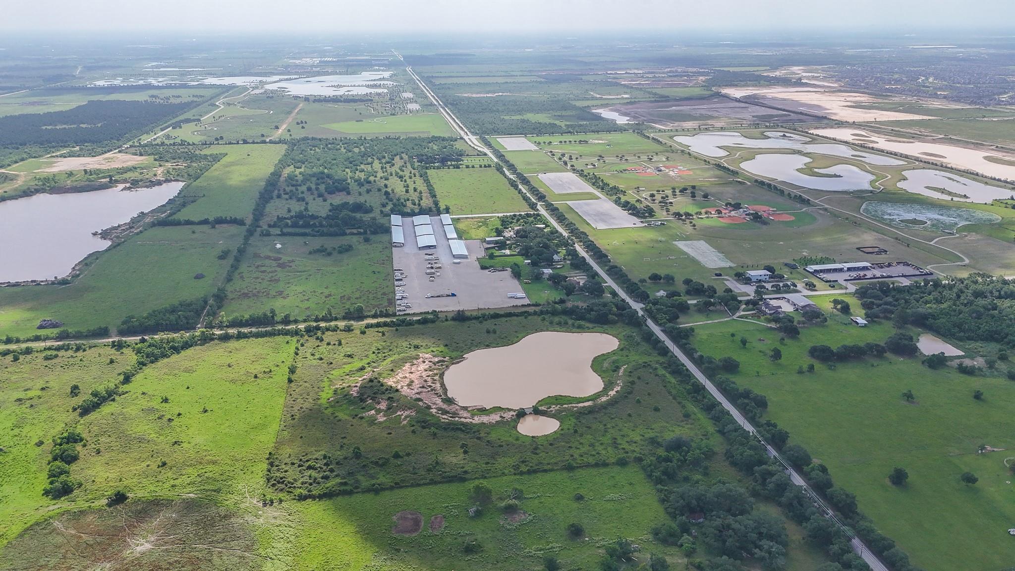 Aerial view of green acreage with several ponds, long outbuildings, and roads.