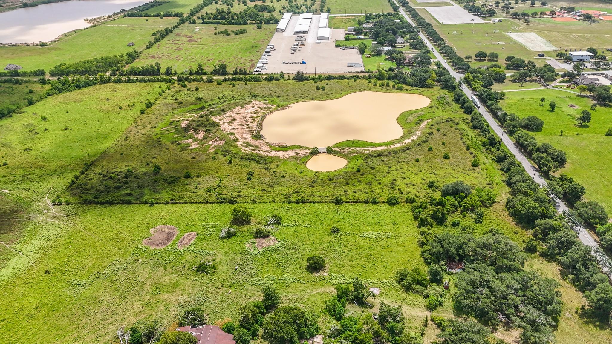 Aerial view of grassy land with two ponds beside a tree-lined road.
