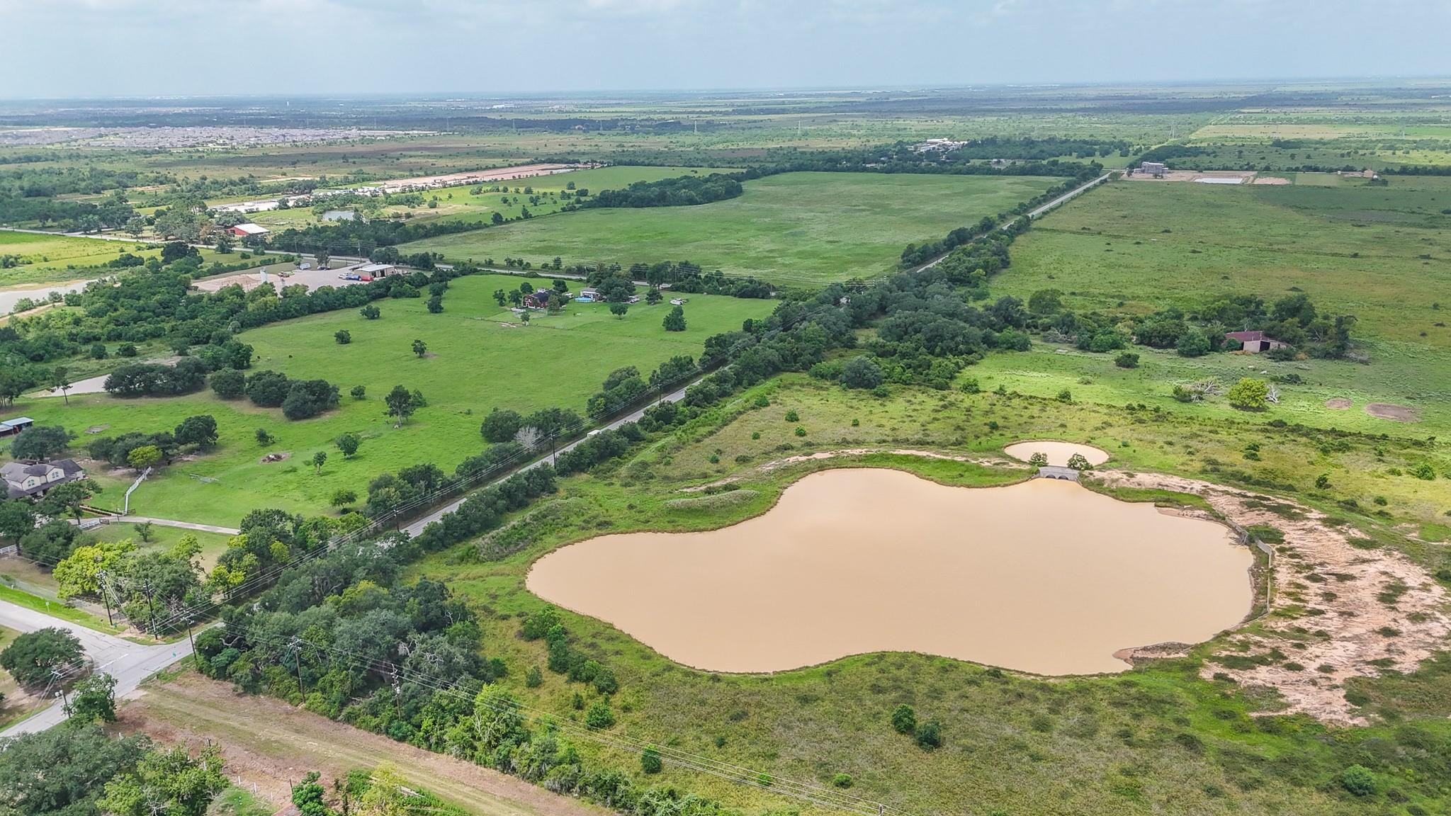 Aerial view of green rural acreage with a large pond, scattered buildings, and roads.