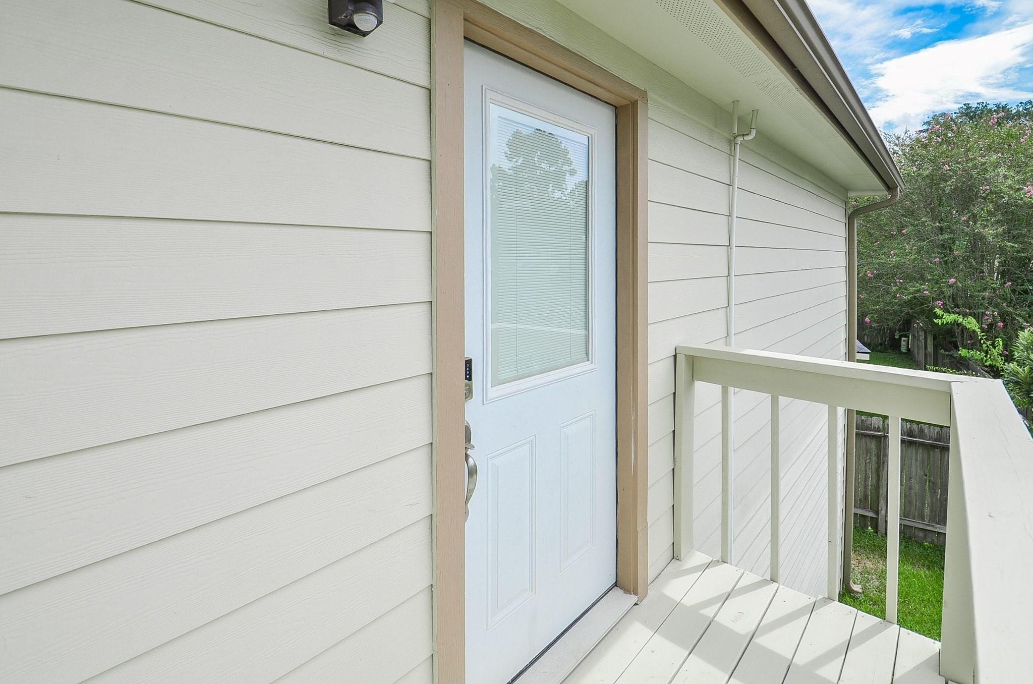 Raised entry porch with a white front door and pale railing overlooking a fenced yard.