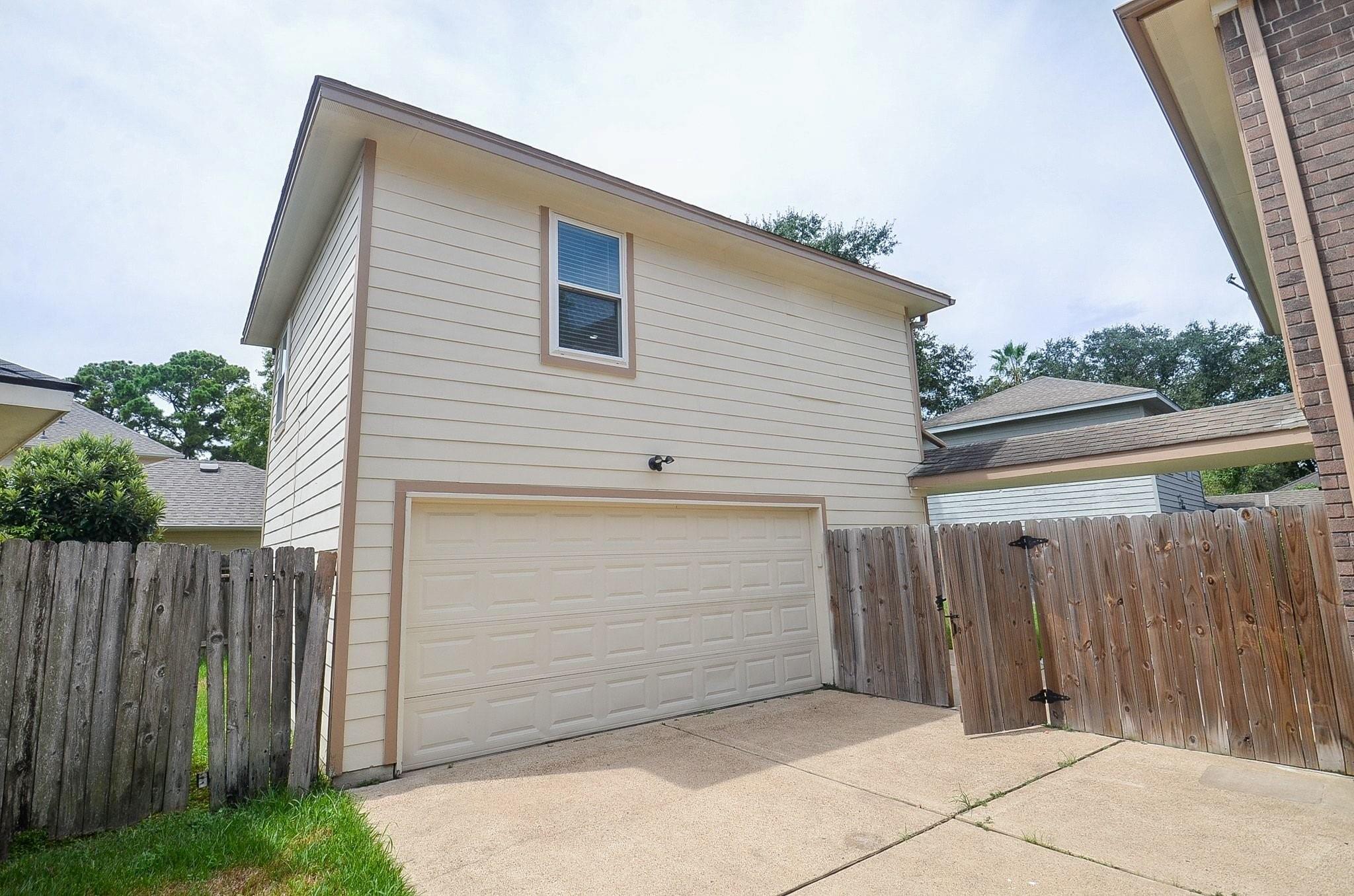 Two-story light-sided garage with a wide double door, concrete driveway, and wooden privacy fencing.