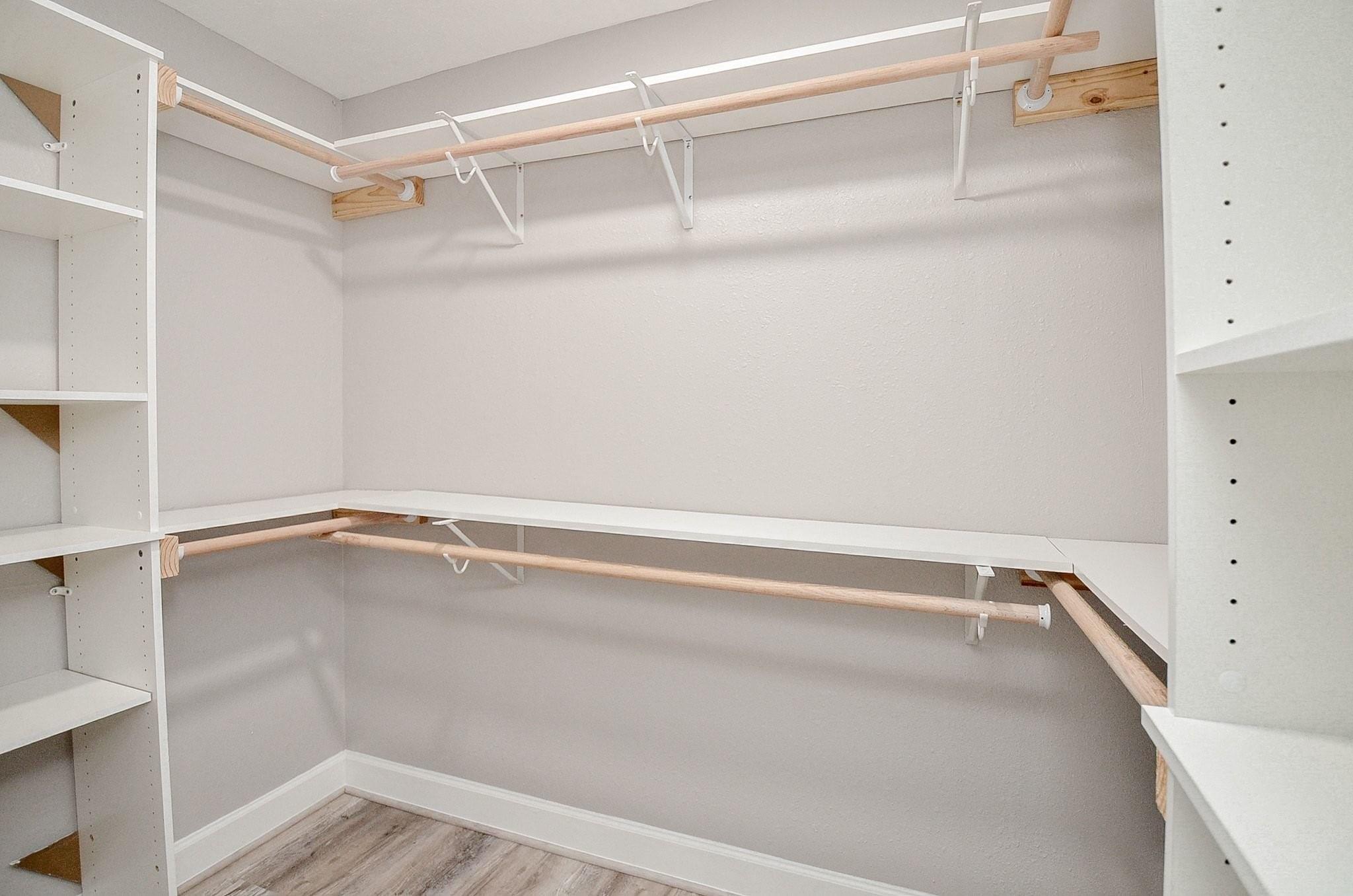 Walk-in closet with built-in shelves, wraparound hanging rods, and wood-look flooring.