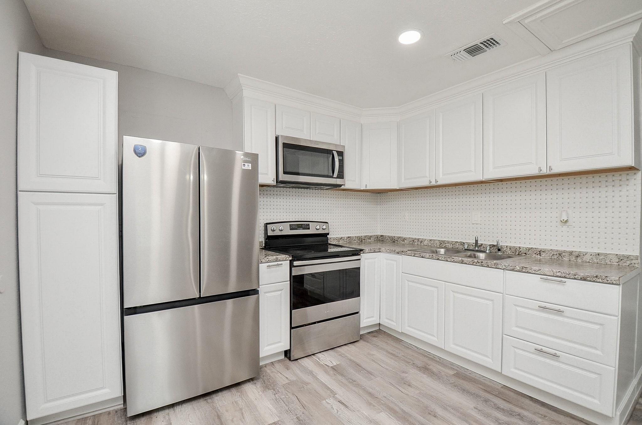 Kitchen with white cabinets, stainless steel appliances, granite counters, and patterned tile backsplash.