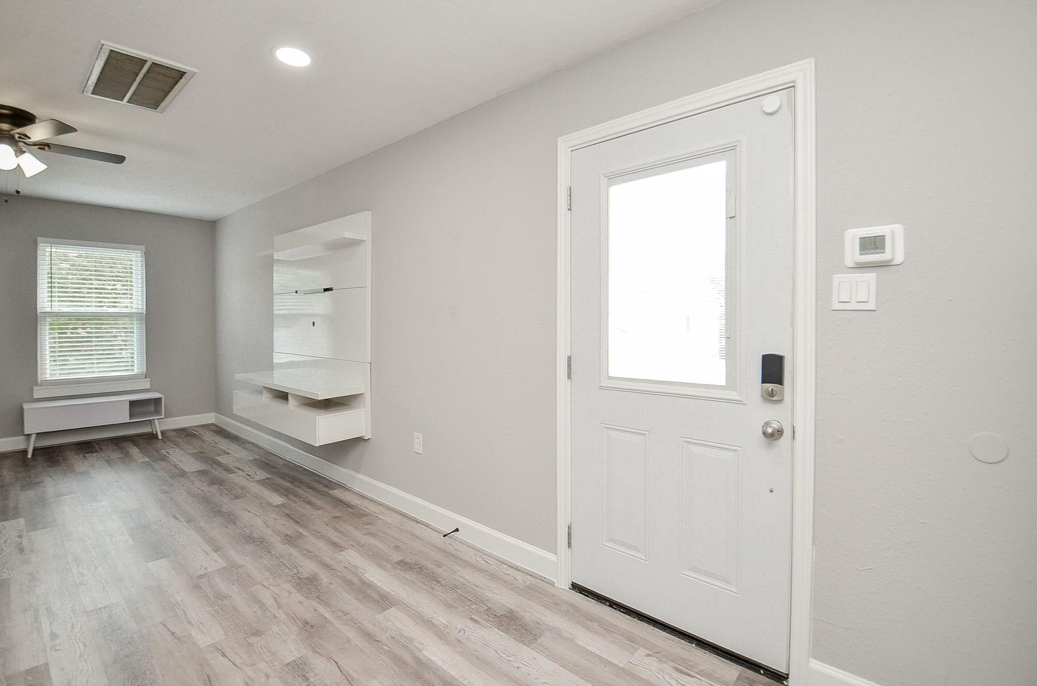 Entry with a white front door, gray wood-look flooring, and built-in shelving beside a window.