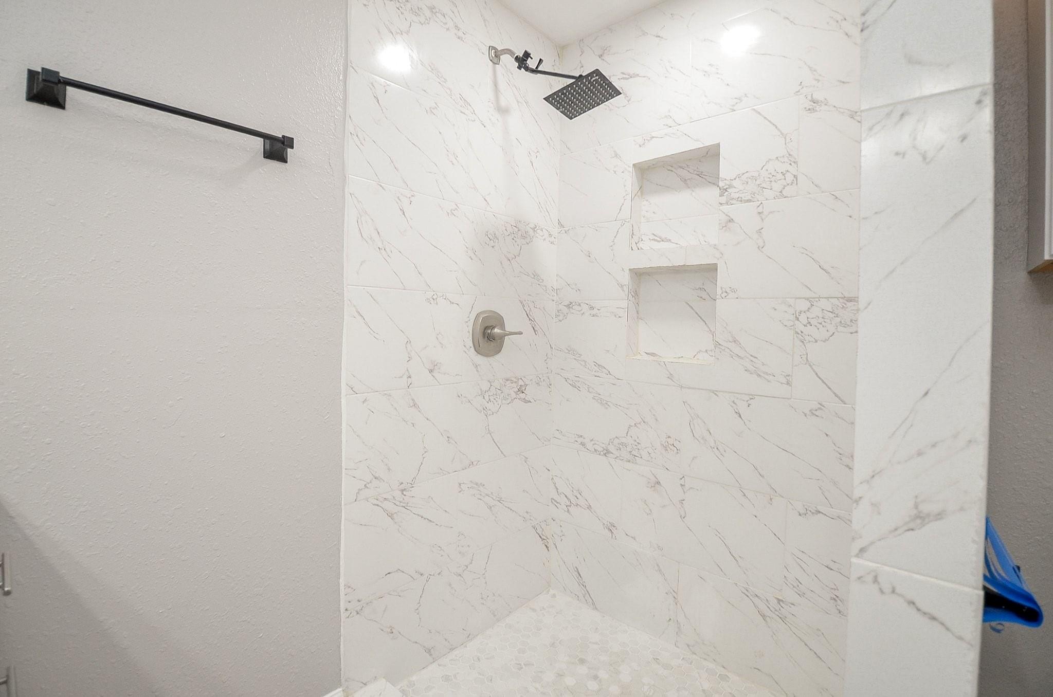Walk-in shower with marble-look tile, two built-in niches, and a square rainfall showerhead.