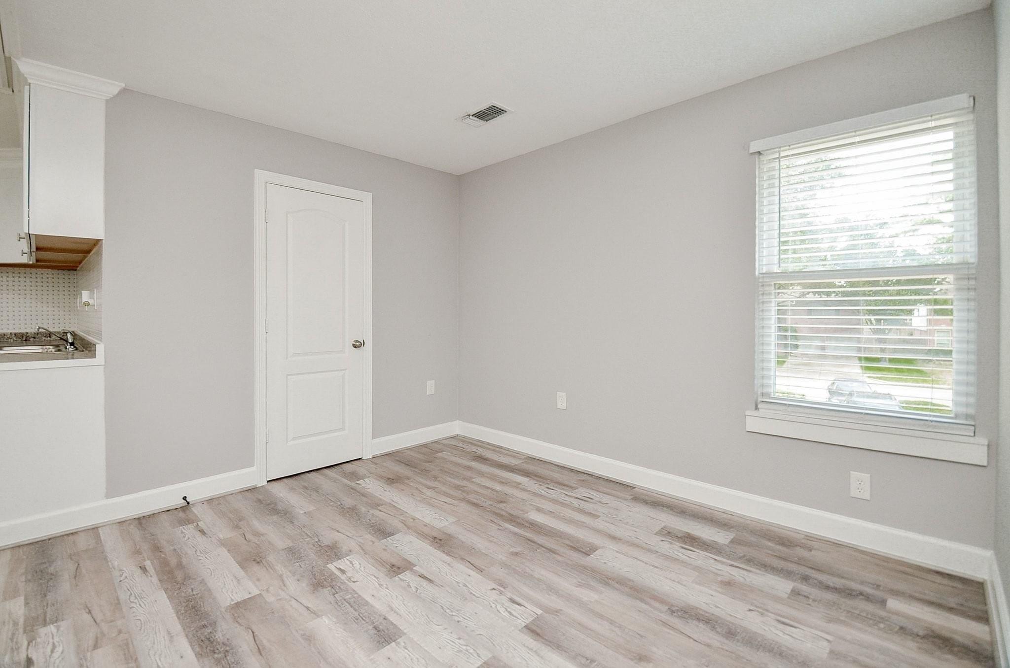 Empty room with gray walls, wood-look plank flooring, and a large window beside the kitchen.