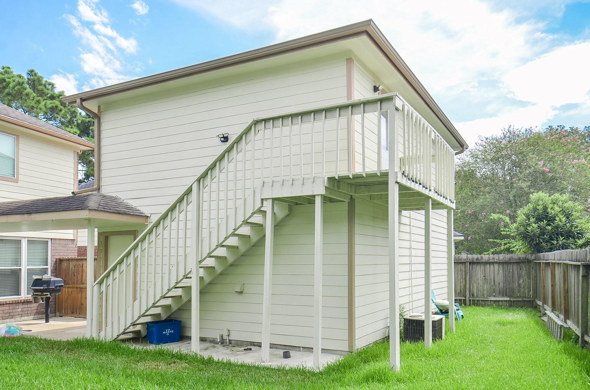 Home’s rear exterior with an elevated deck, long staircase, and fenced grassy backyard.