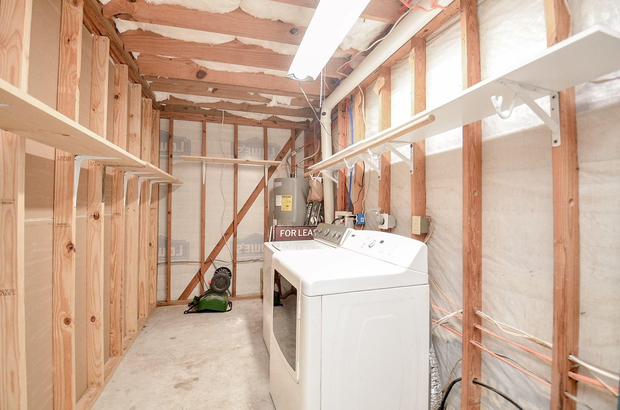 Unfinished laundry room with a white washer and dryer, exposed framing, and wall-mounted hanging rails.