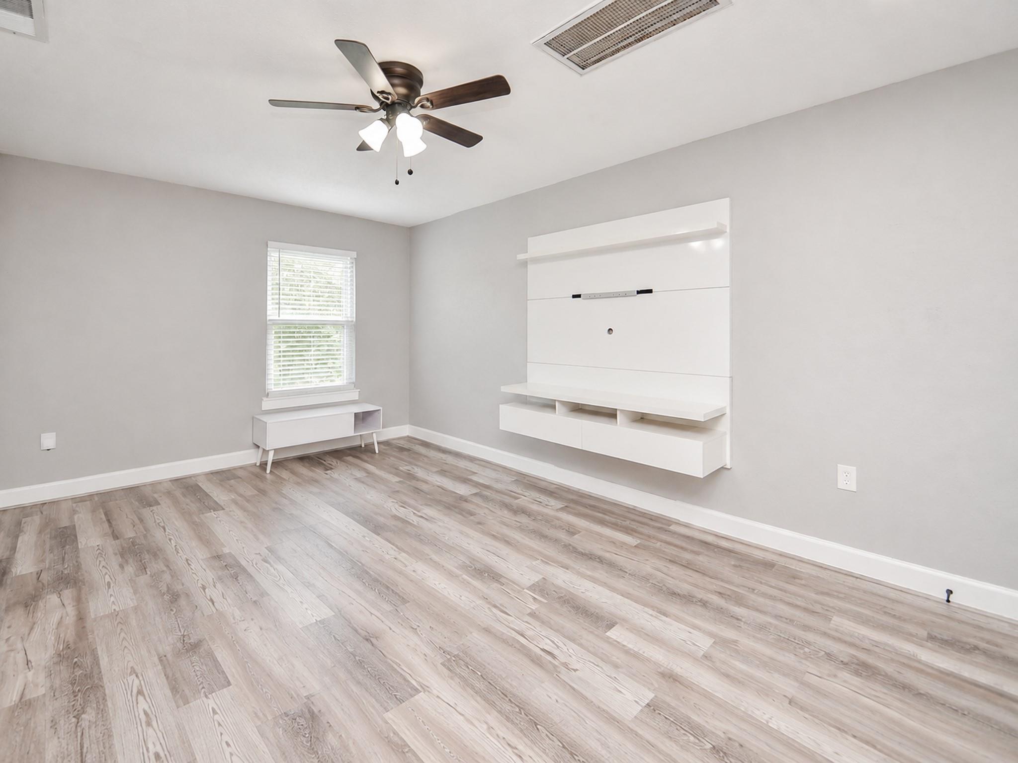 Bright room with a white built-in media center, window with blinds, and wood-look flooring.