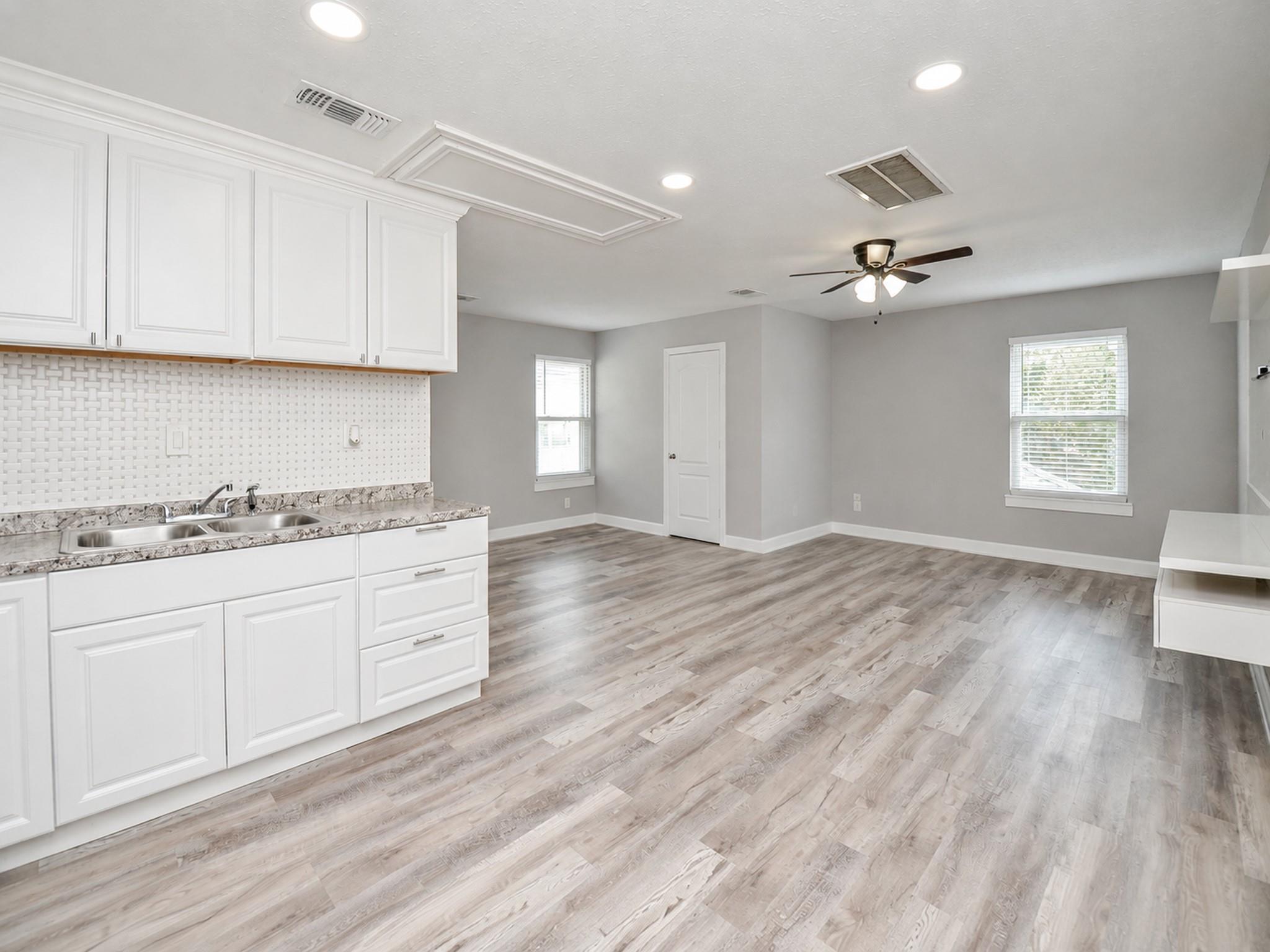 Open kitchen and living area with white cabinets, gray wood-look flooring, and a ceiling fan.