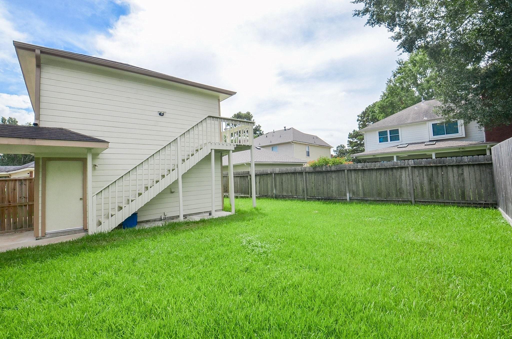 Backyard with a broad green lawn, elevated exterior stairs, and a wooden privacy fence.