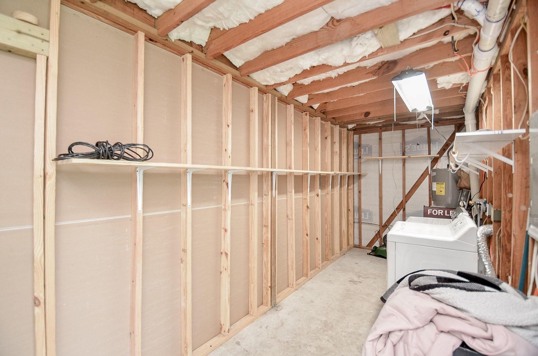 Unfinished utility room with exposed framing, a washer, HVAC equipment, and a long wall shelf.