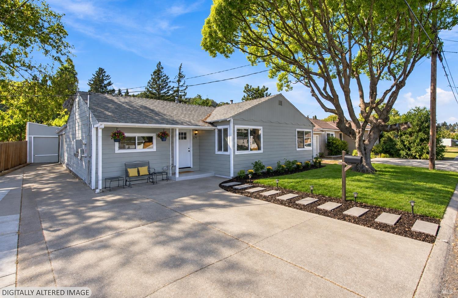Gray single-story house with a broad driveway, mature shade tree, and stepping-stone garden path.