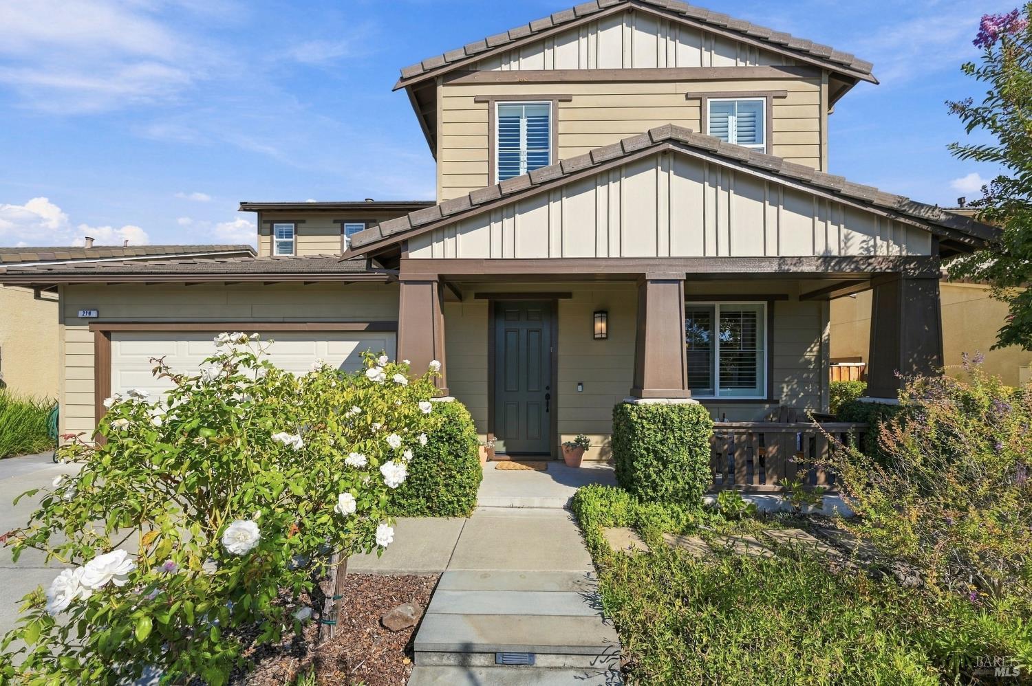 218 Saffron Court, a two-story beige home with a covered porch, attached garage, and white roses.