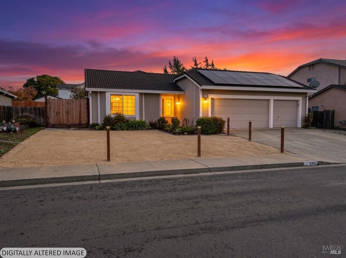 Single-story house with rooftop solar panels and a two-car garage beneath a colorful dusk sky.