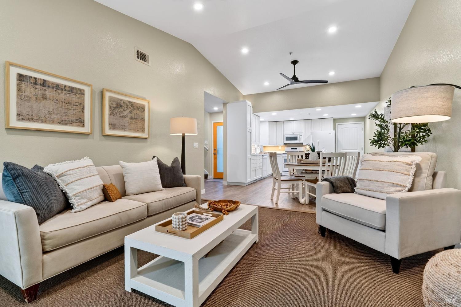 Open-plan living room with cream sofas, a white coffee table, and a kitchen beyond.