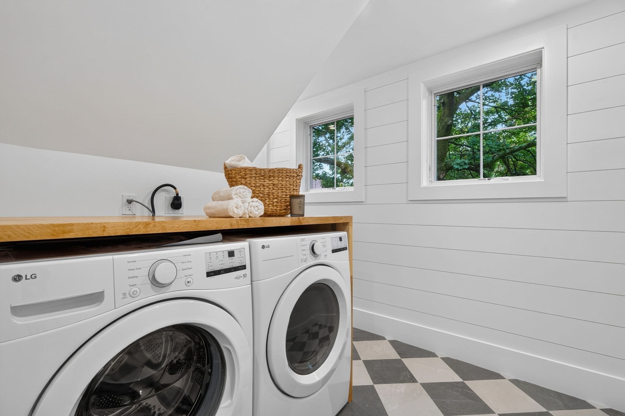 Laundry room with front-loading washer and dryer, wooden countertop, two windows, and checkerboard floor.