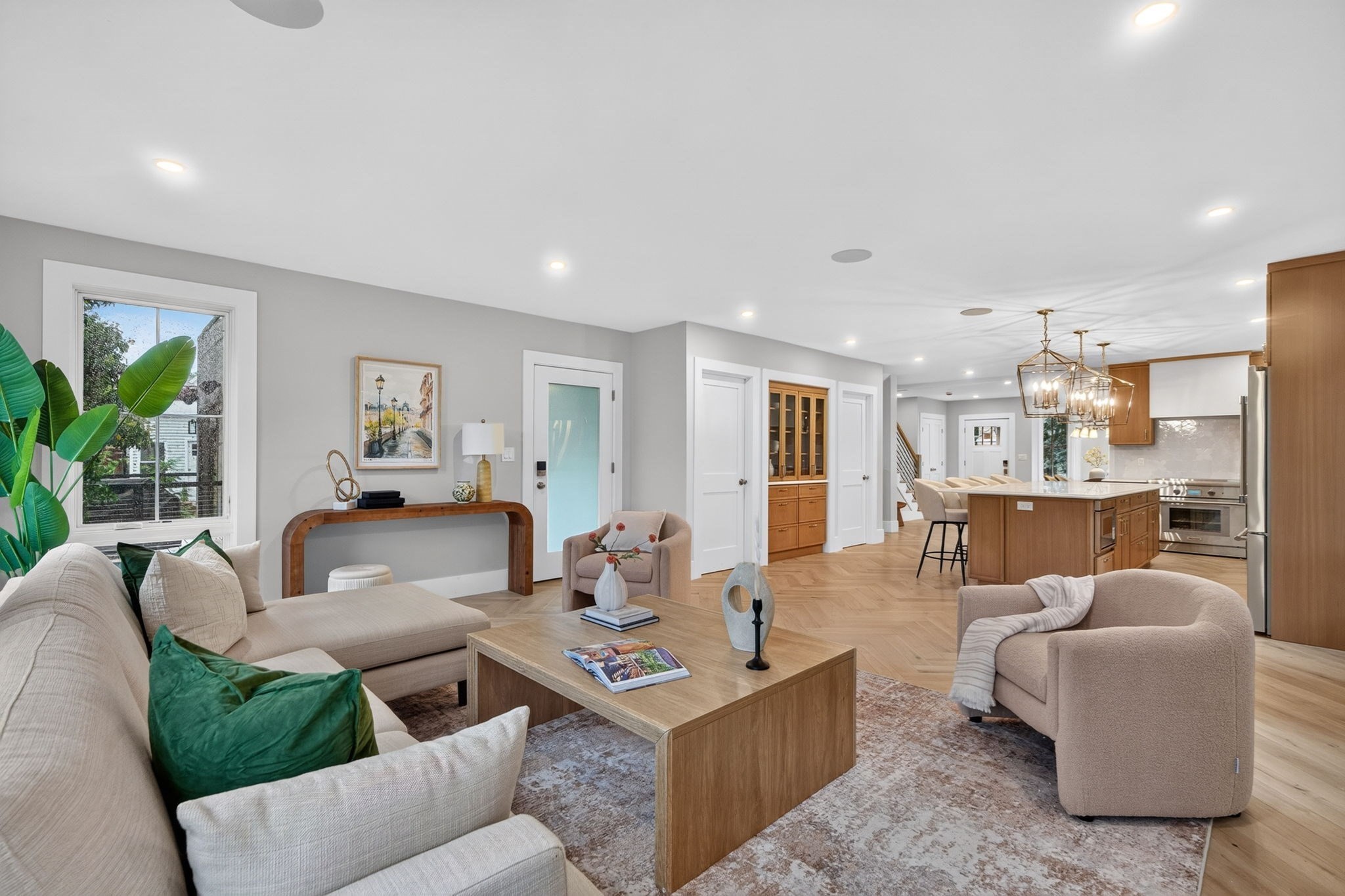 Open-plan living room and kitchen with neutral sofas, a wood coffee table, and a wood-cabinet island.