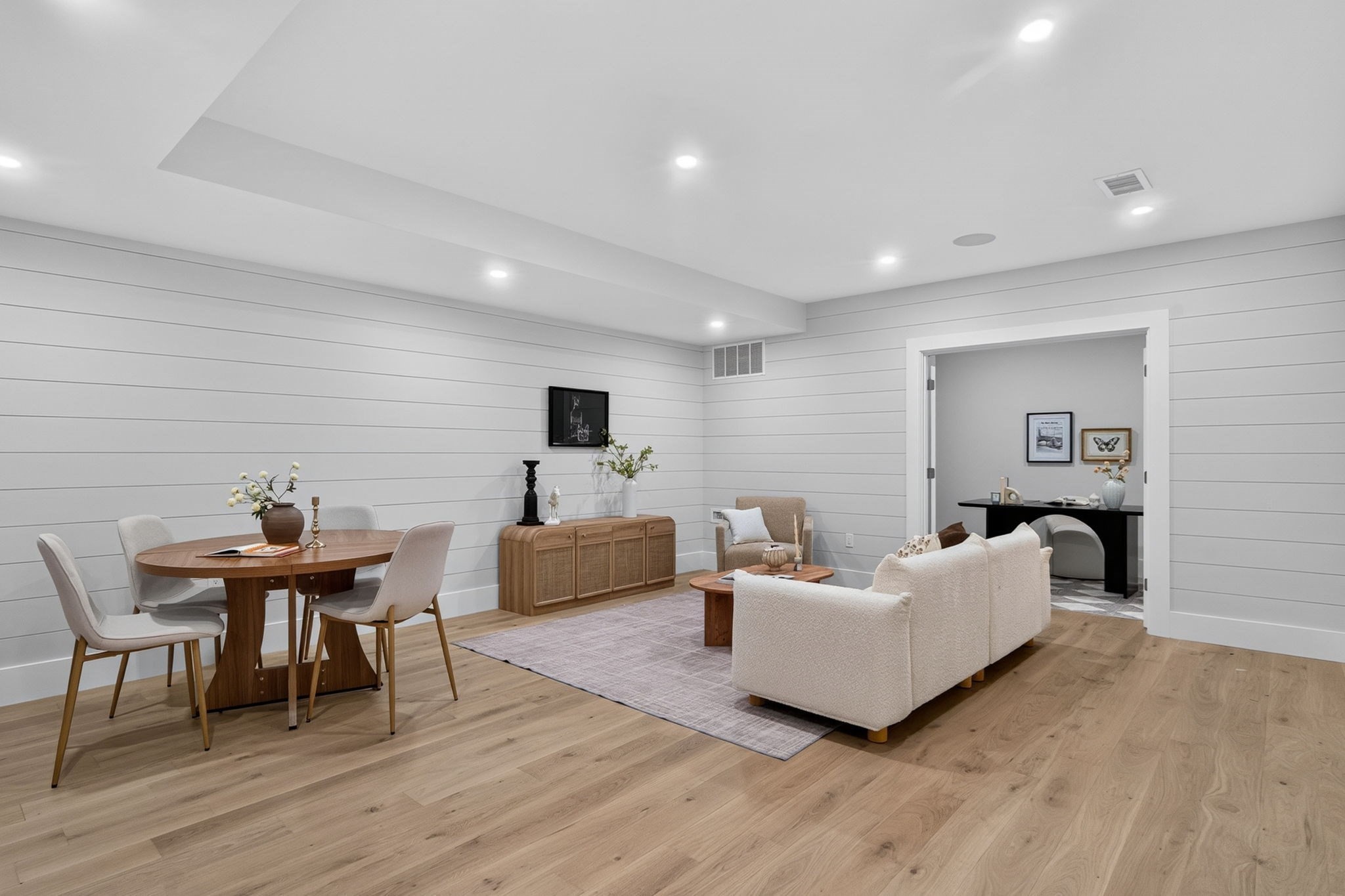 Open-plan living and dining room with white shiplap walls and cream seating.