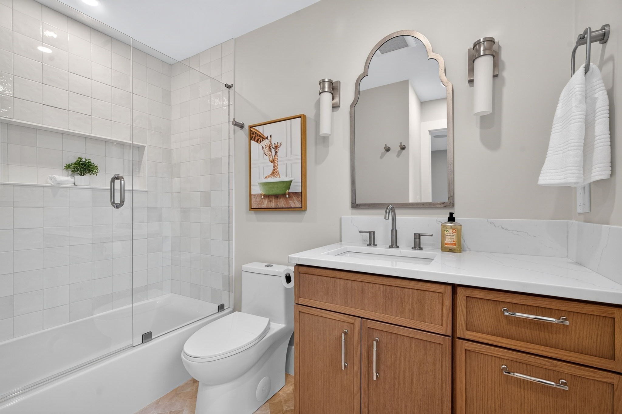 Bathroom with a glass-enclosed tiled tub and shower, wood vanity, and arched mirror.