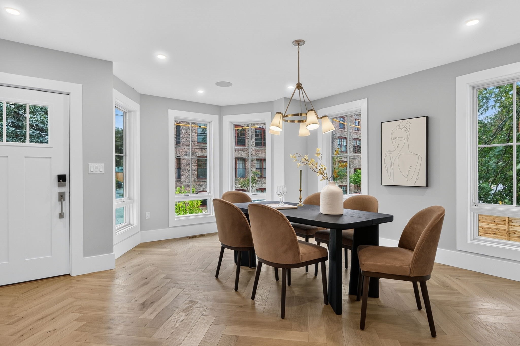 Dining room with a black table, brown chairs, brass chandelier, and large windows.