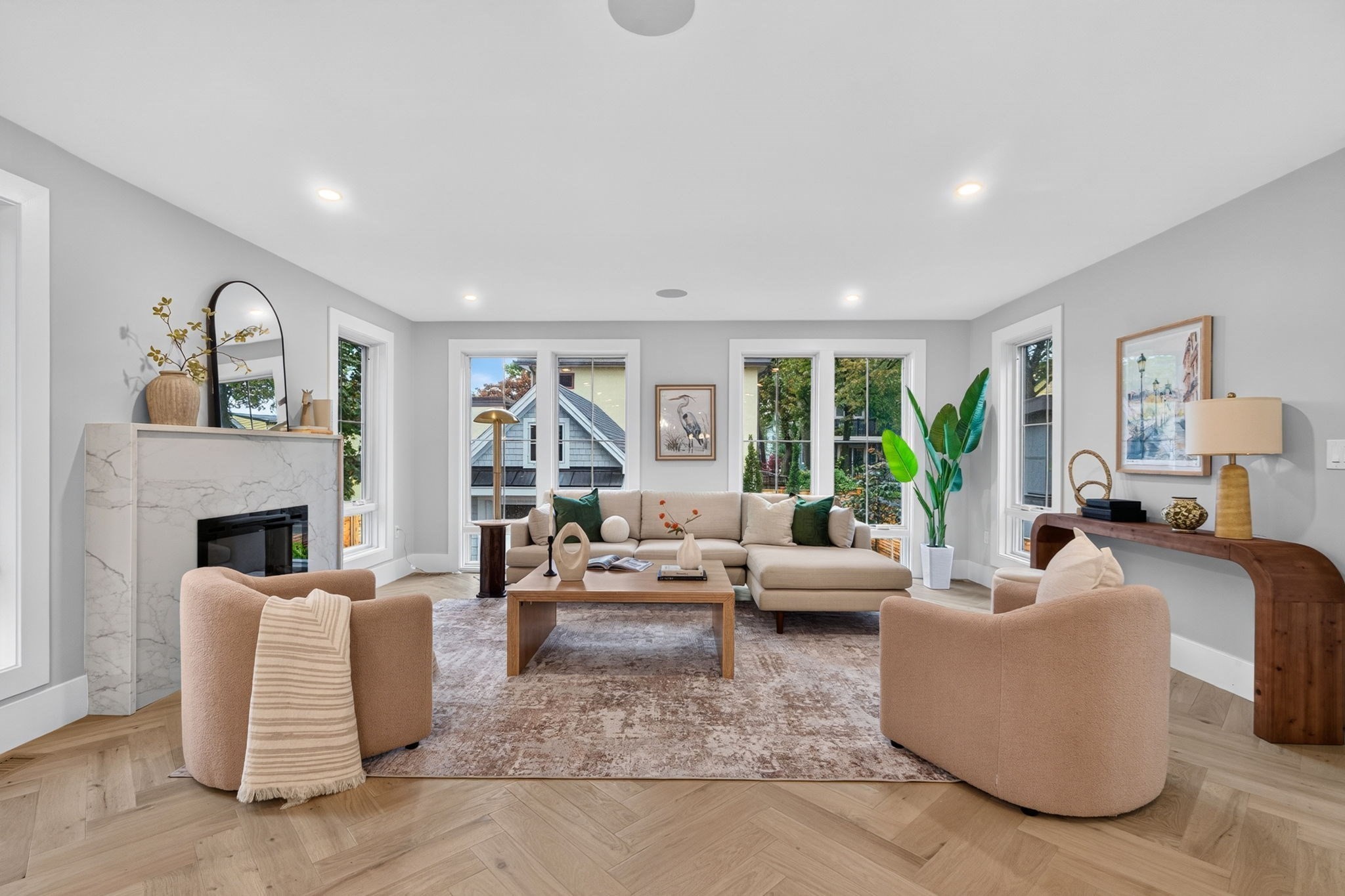Living room with a marble fireplace, beige sectional, rounded chairs, and large windows.