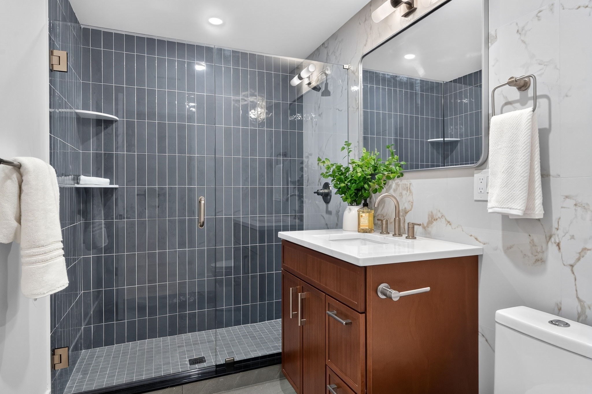 Bathroom with a dark gray tiled walk-in shower and a wood vanity topped by a white sink.