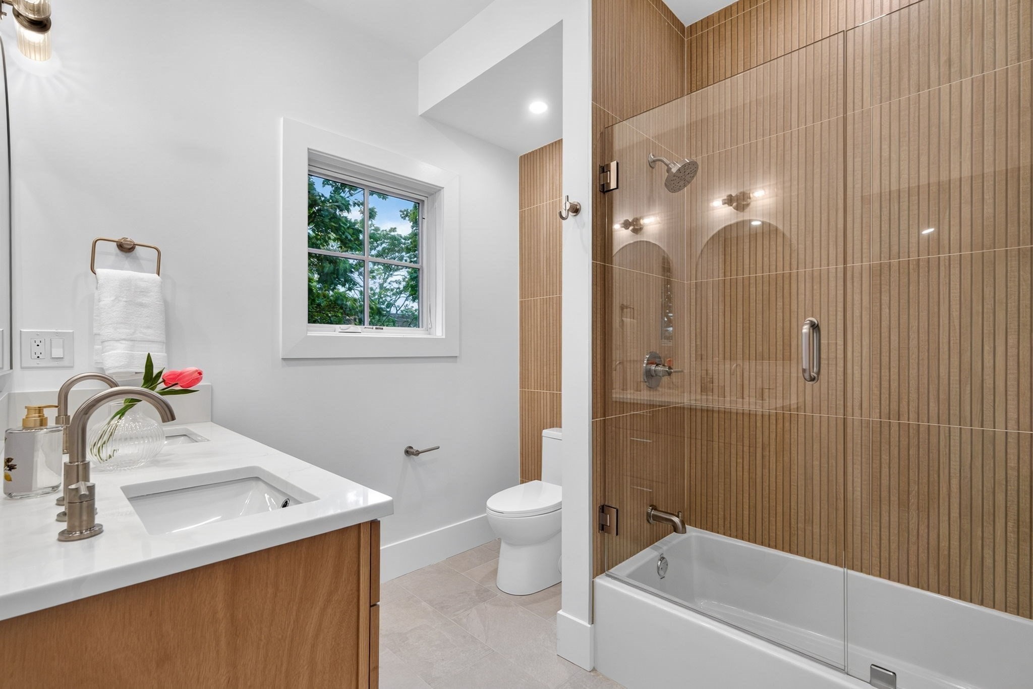 Modern bathroom with a wood-front vanity and bathtub behind a glass screen with wood-look tile.