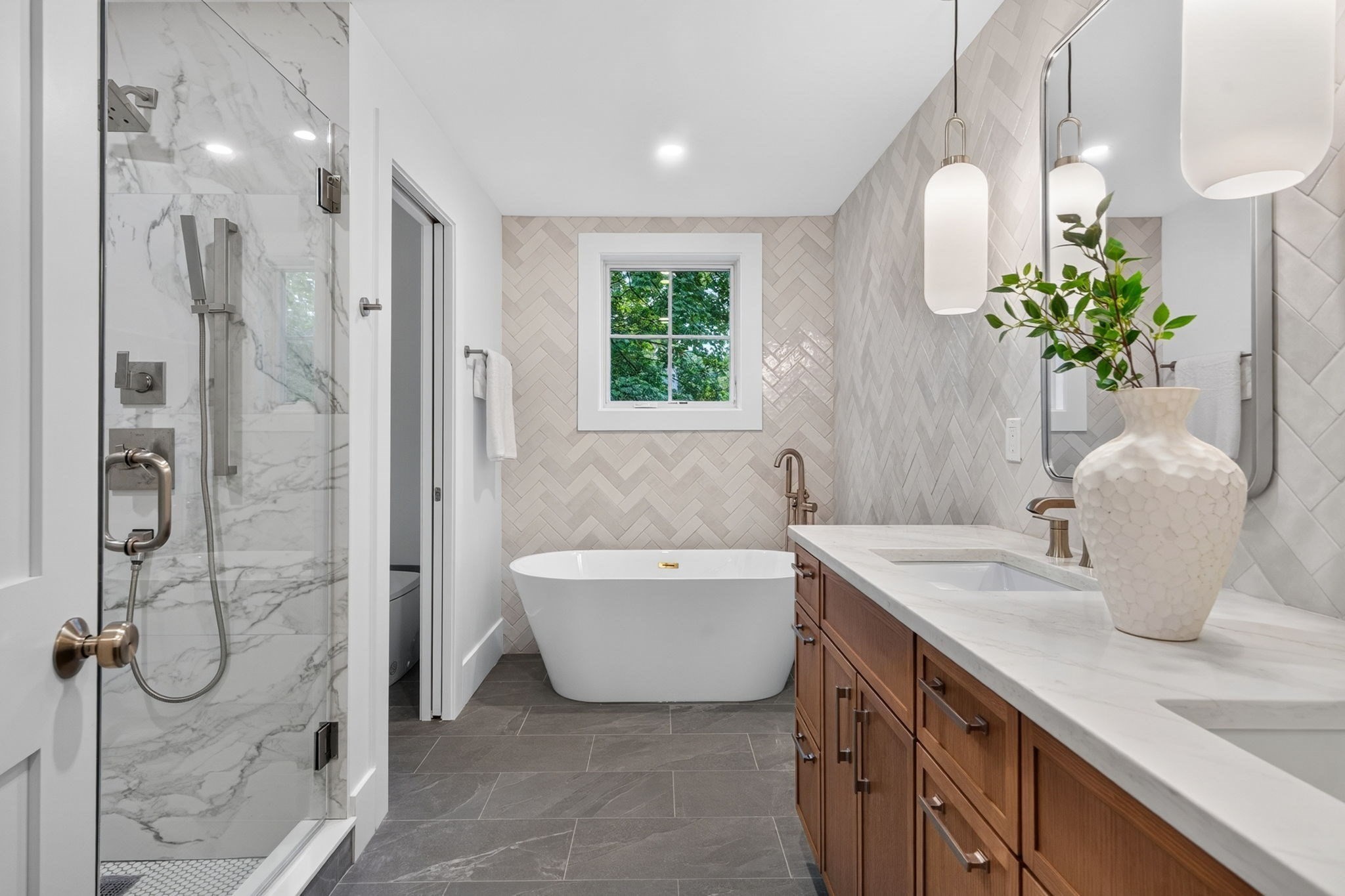 Bathroom with a marble shower, freestanding tub, herringbone tile, and warm wood double vanity.