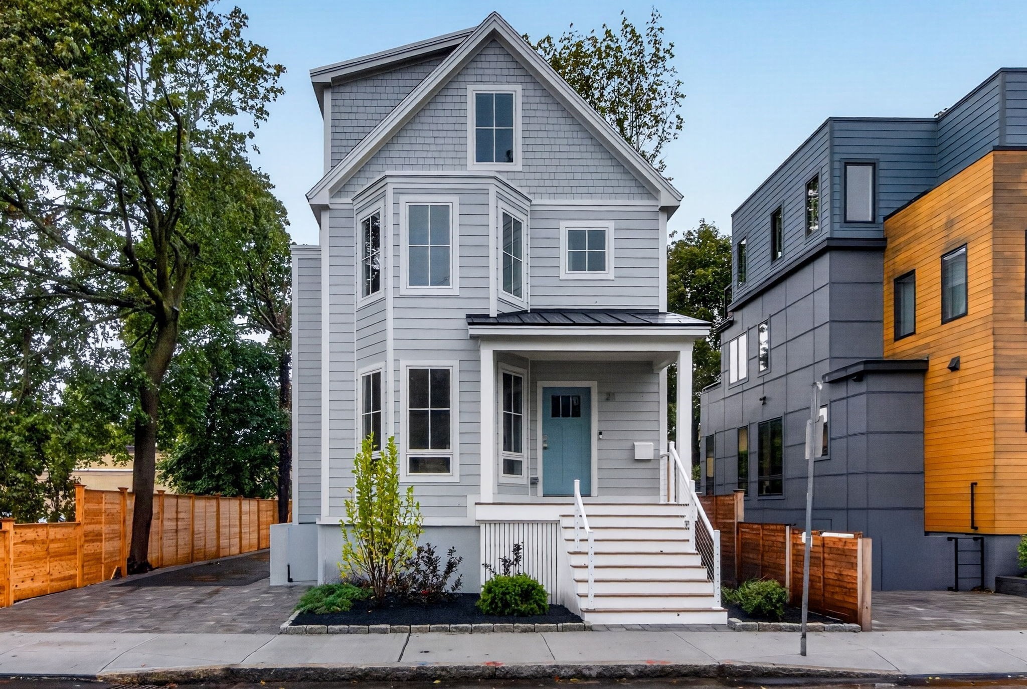Gray gabled house with a blue front door, white porch steps, and landscaped entry garden.
