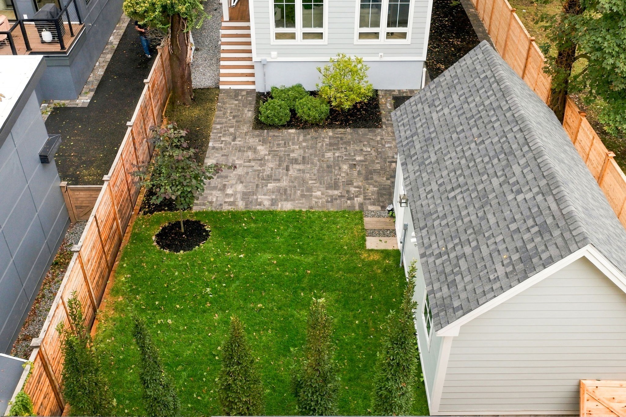 Aerial backyard with a large lawn, paved patio, wooden fencing, and detached garage.