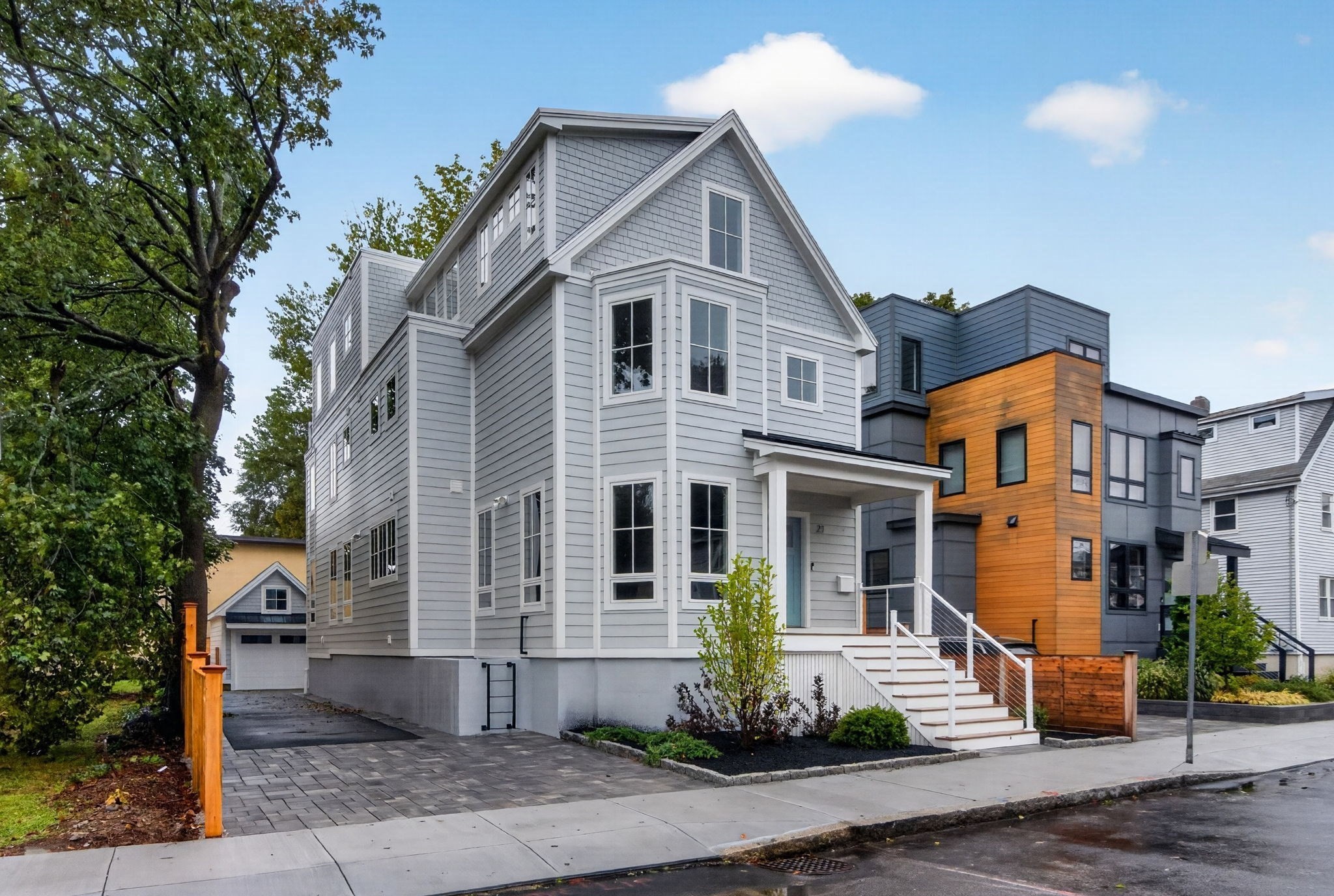 Gray multi-story house with white trim and front steps, beside a modern home with orange wood siding.