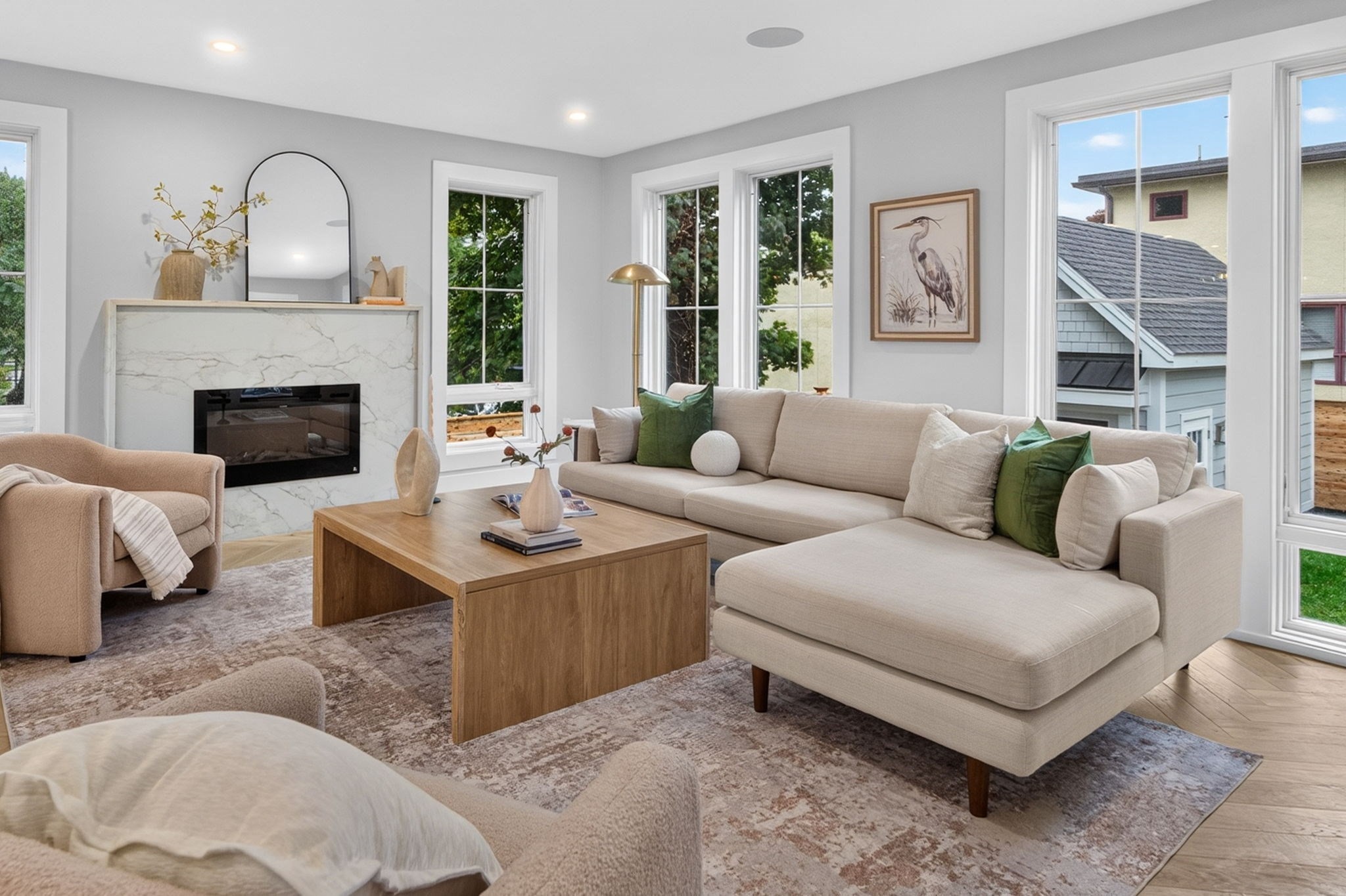 Staged living room with a marble fireplace, cream sectional, large windows, and wood coffee table.