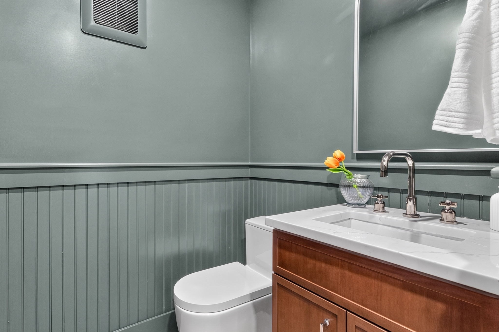Bathroom with sage-green beadboard, a wood vanity, white sink, and orange tulips.