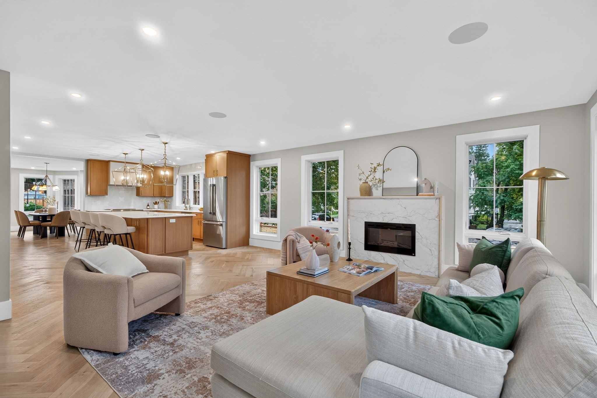 Open-plan living room with a marble fireplace, wood kitchen cabinetry, and large windows.