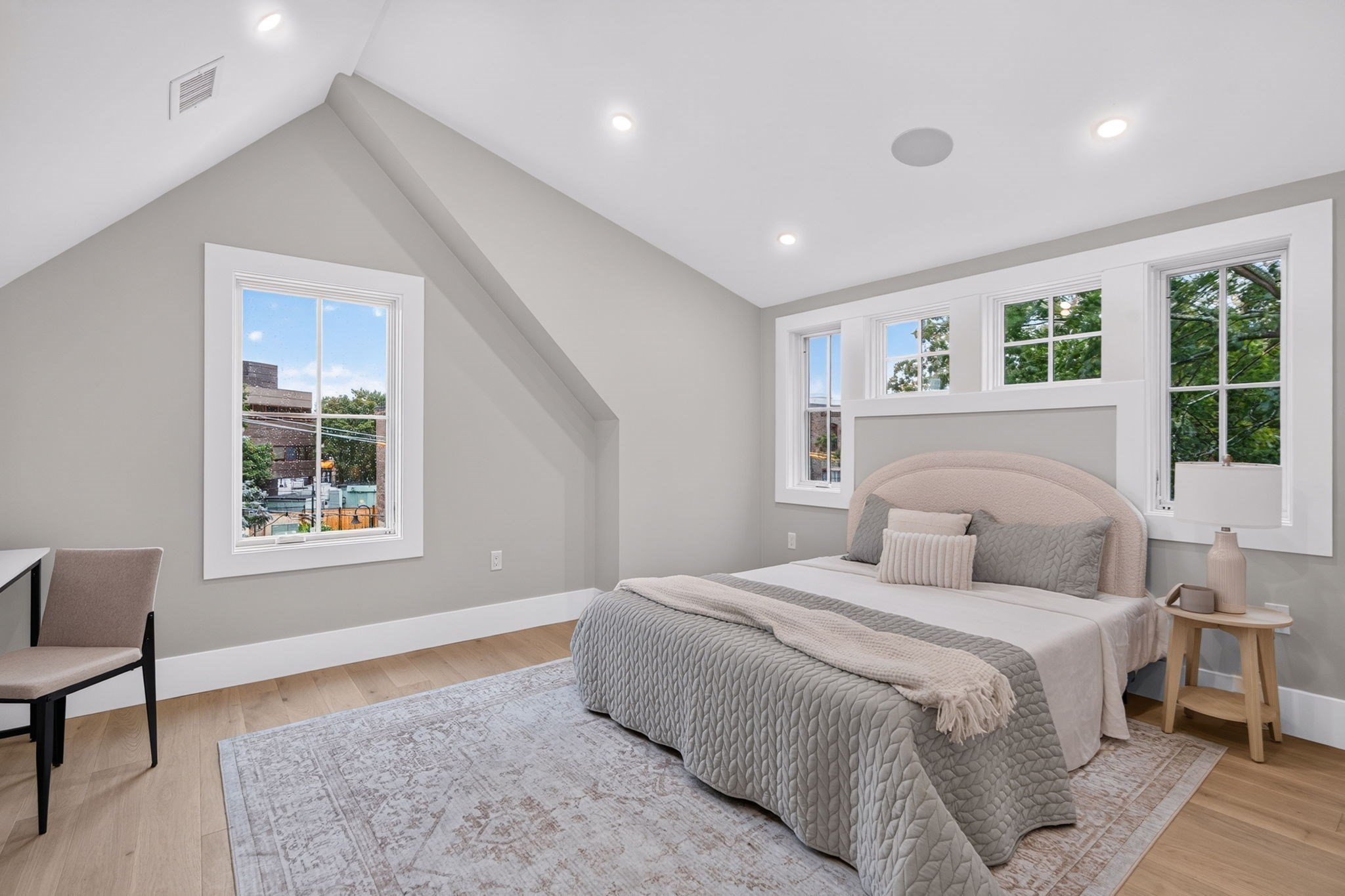 Furnished bedroom with a curved upholstered bed, high sloped ceiling, and multiple windows.