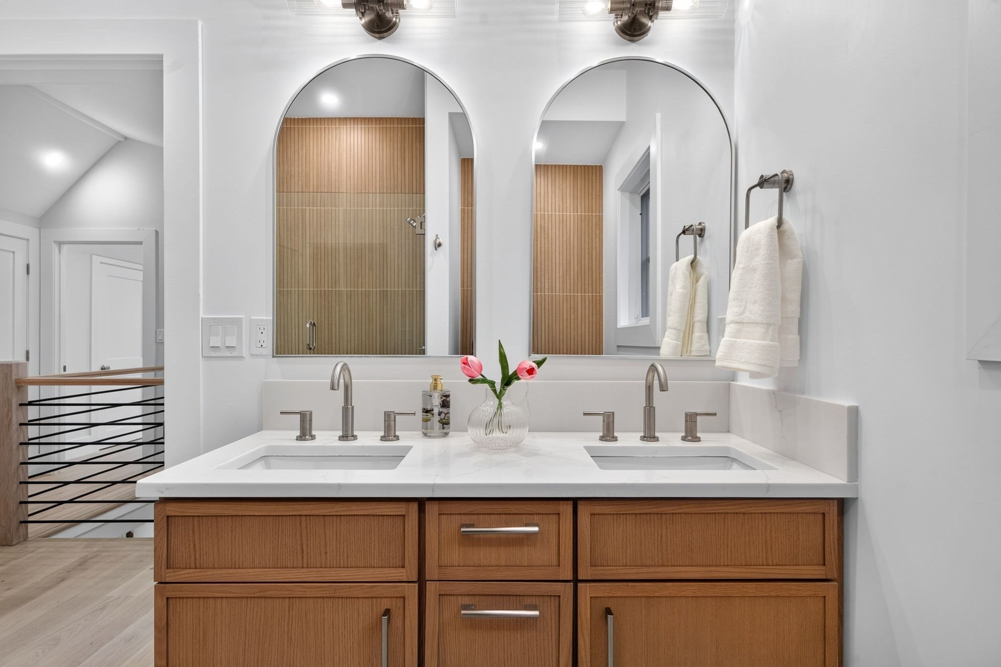 Bathroom with double sinks, warm wood vanity, arched mirrors, and a wood-paneled shower.