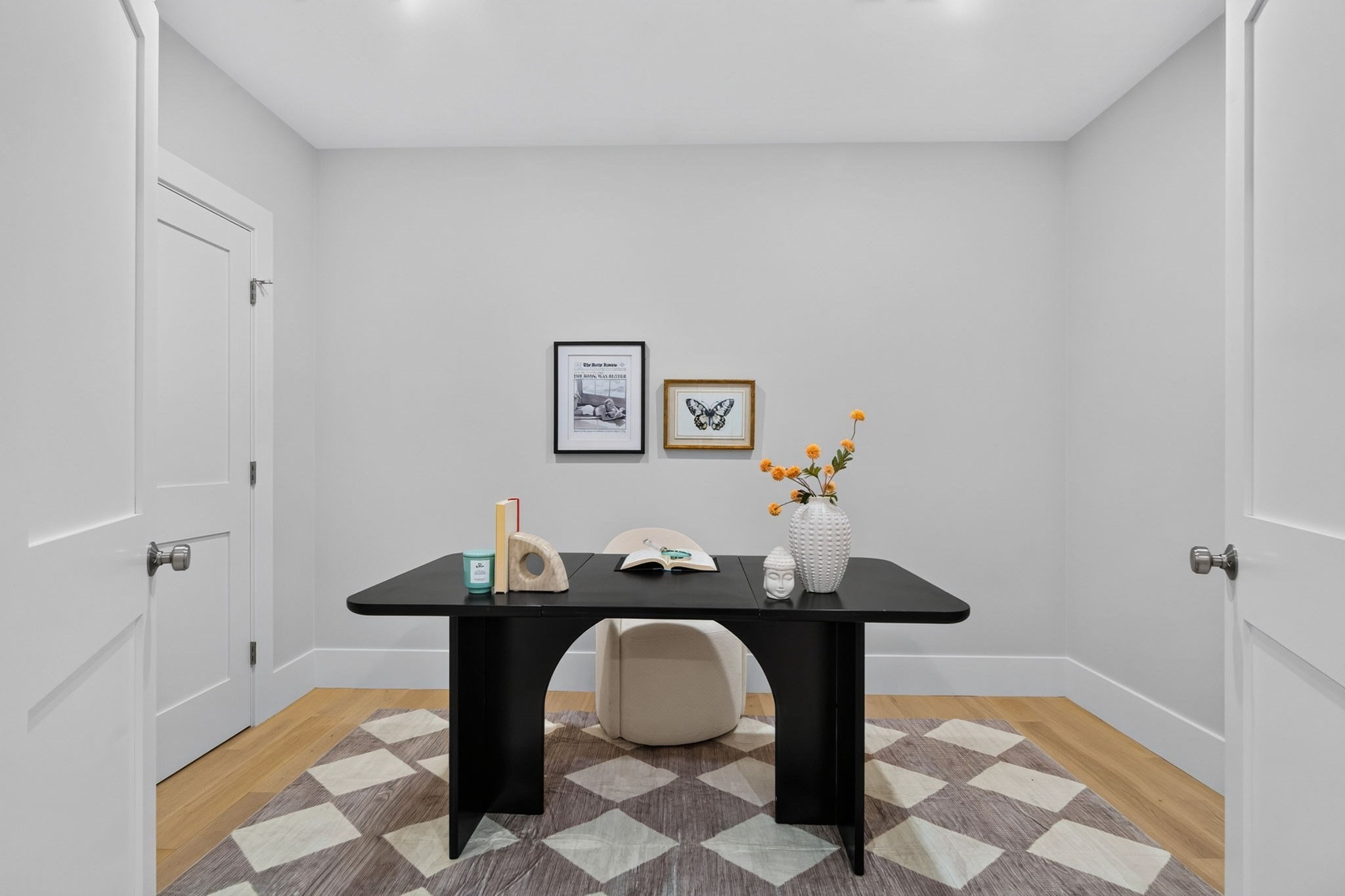 Furnished home office with a black desk, cream chair, geometric rug, and orange flowers.